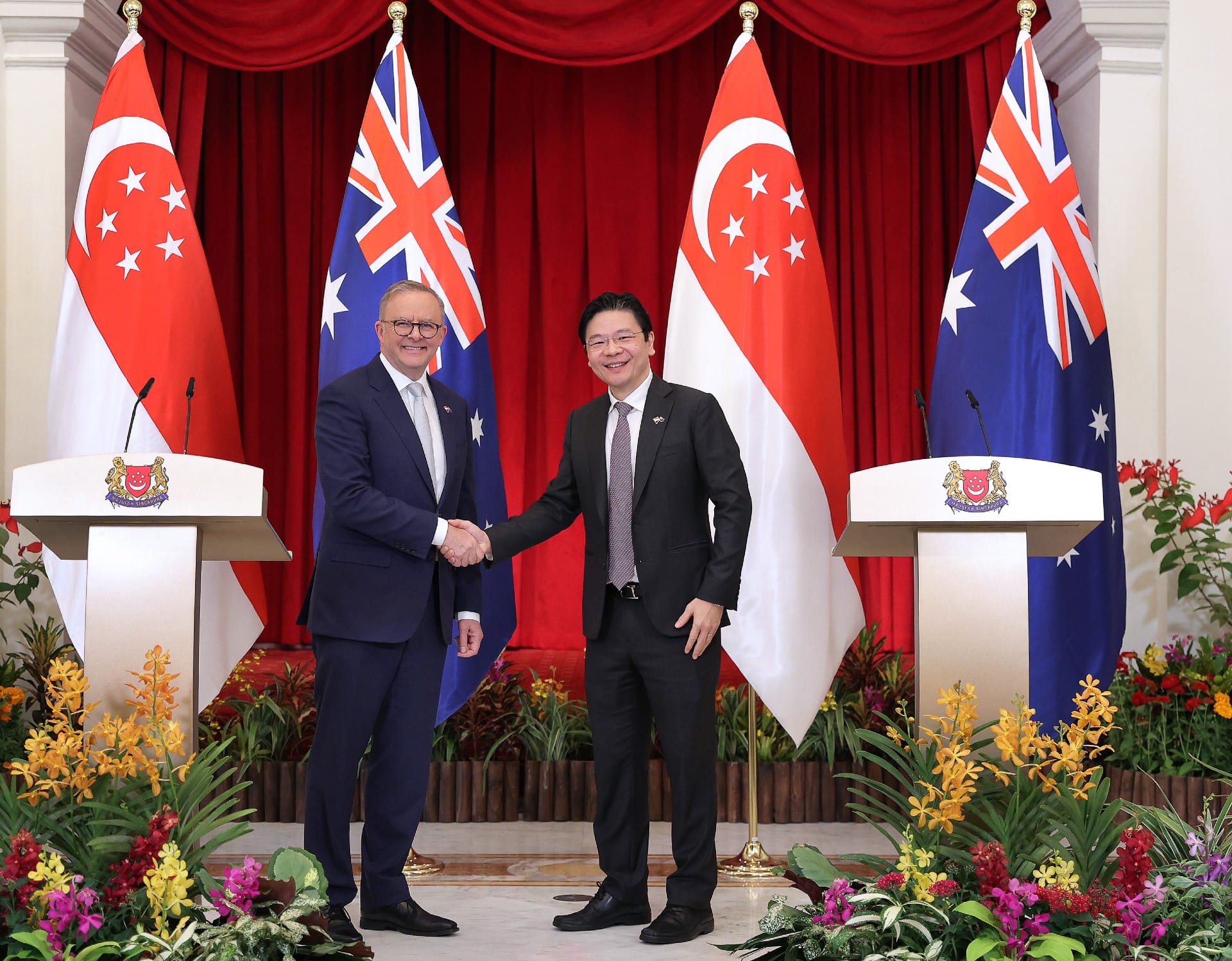 Two men in suits shake hands before Singapore and Australia flags.