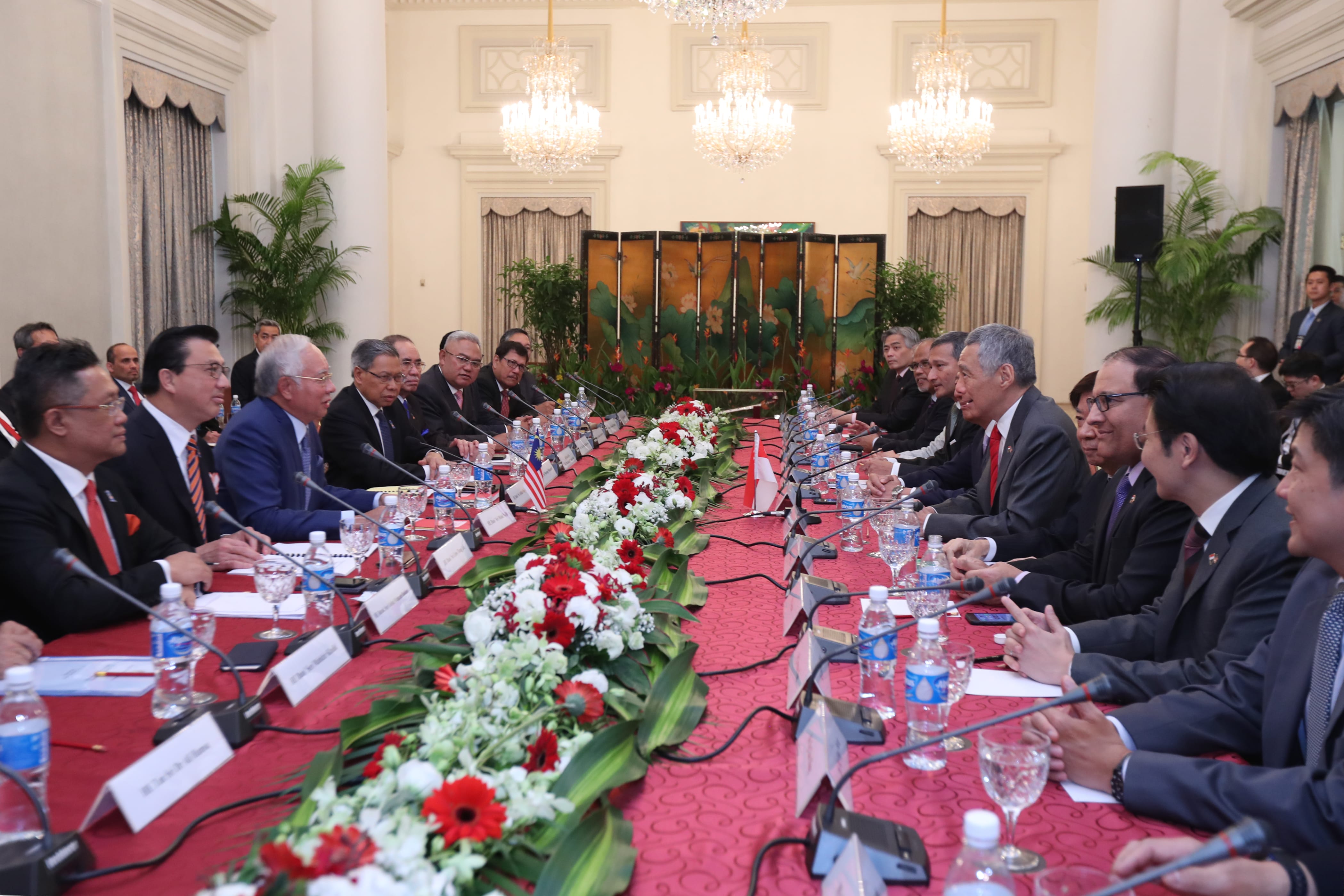 Dignitaries seated at long table, microphones and floral centerpiece.