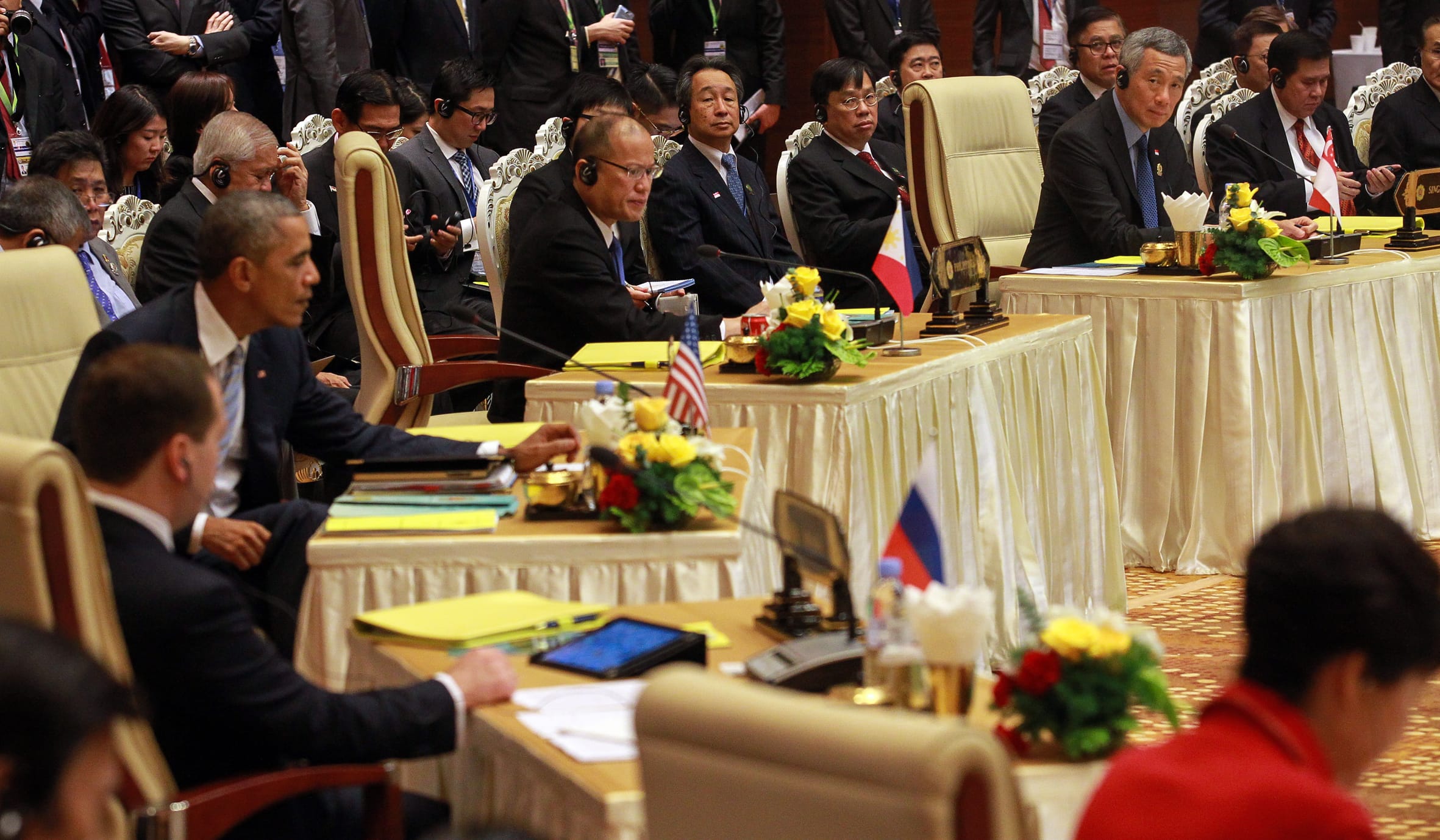Obama at a conference table, with national flags of Philippines, Russia and USA.