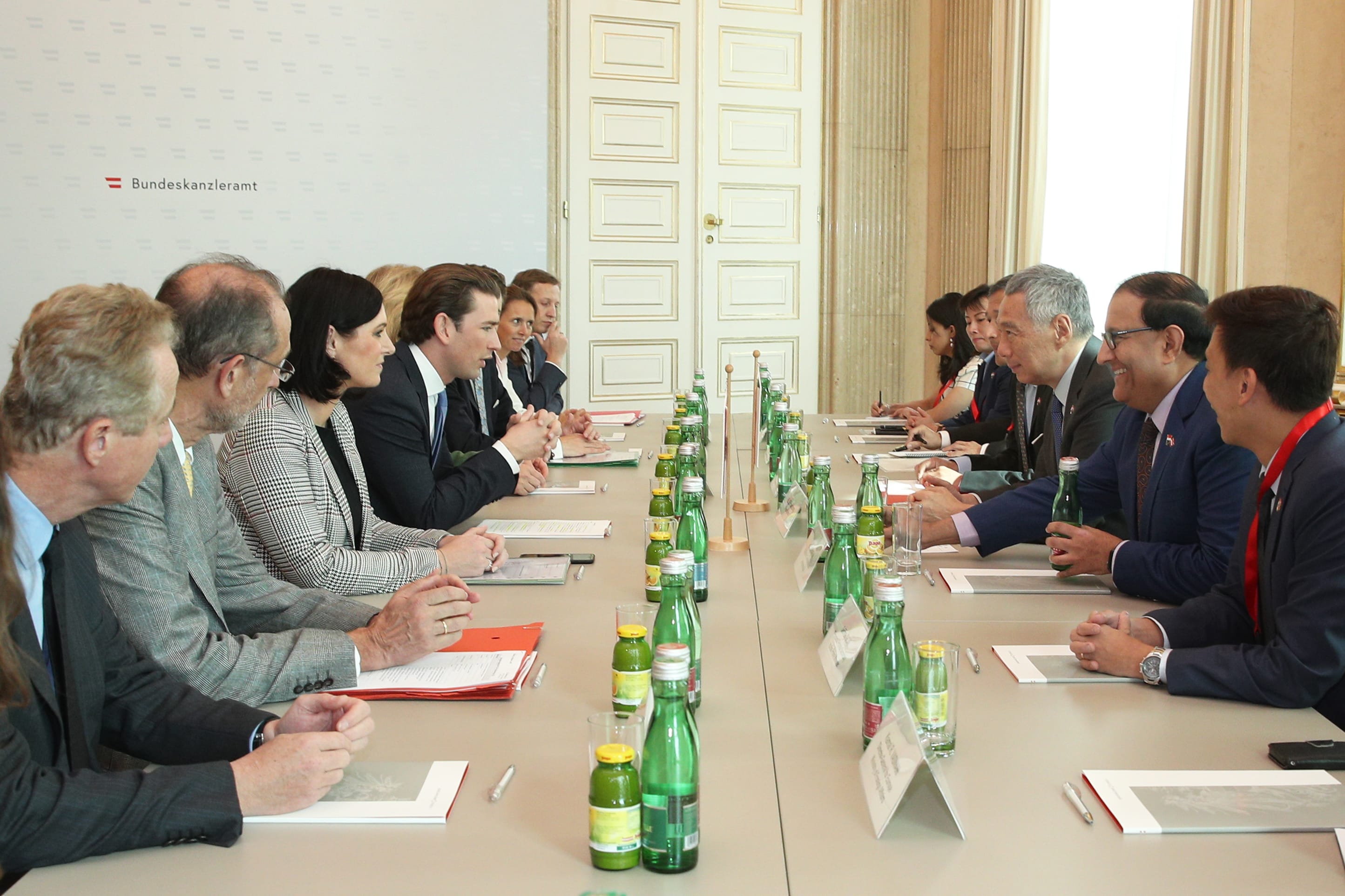 People in business attire seated at long table with water bottles and papers.