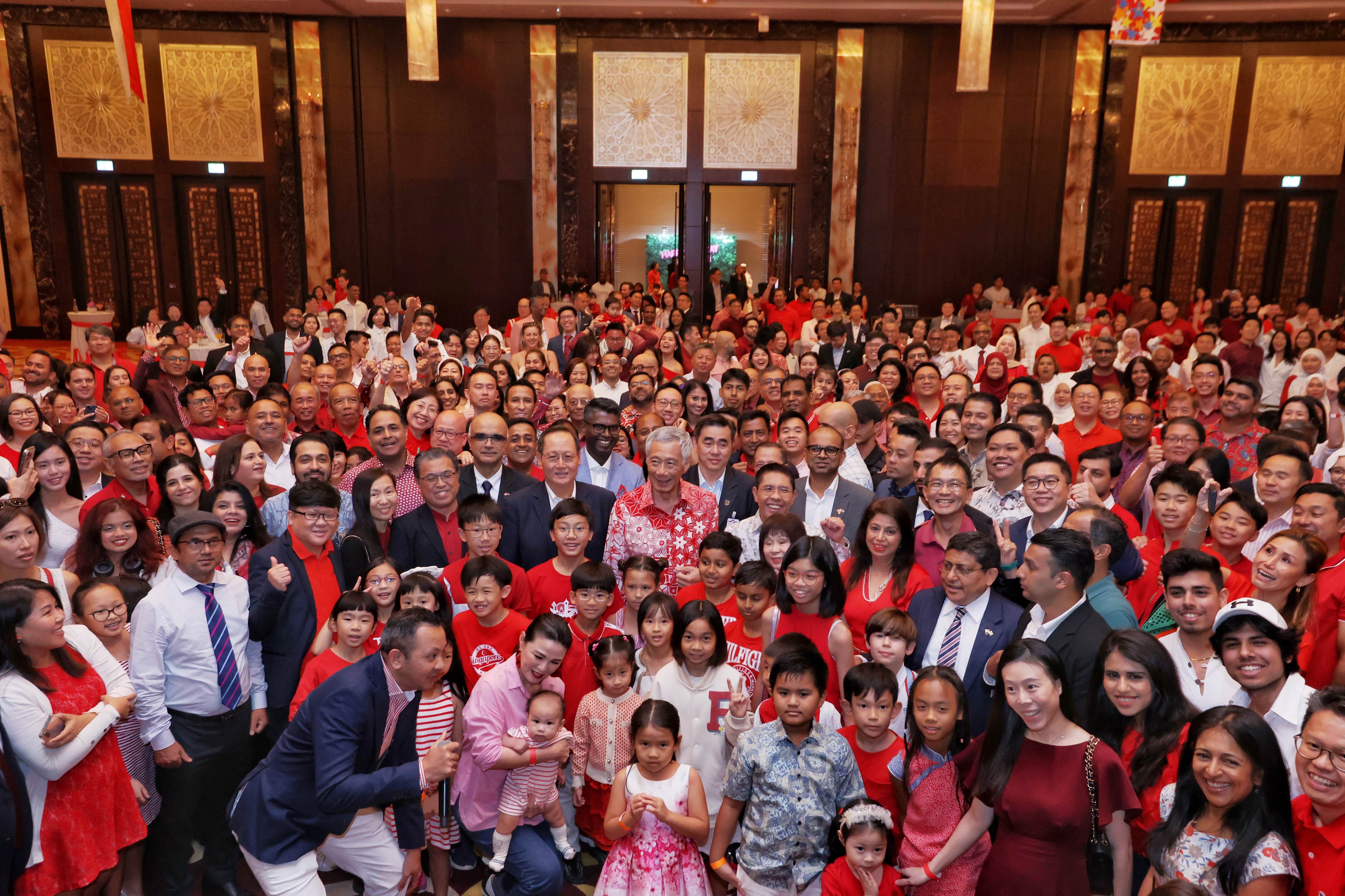Large group of people, many in red, pose in ornate hall; Lee Hsien Loong visible.