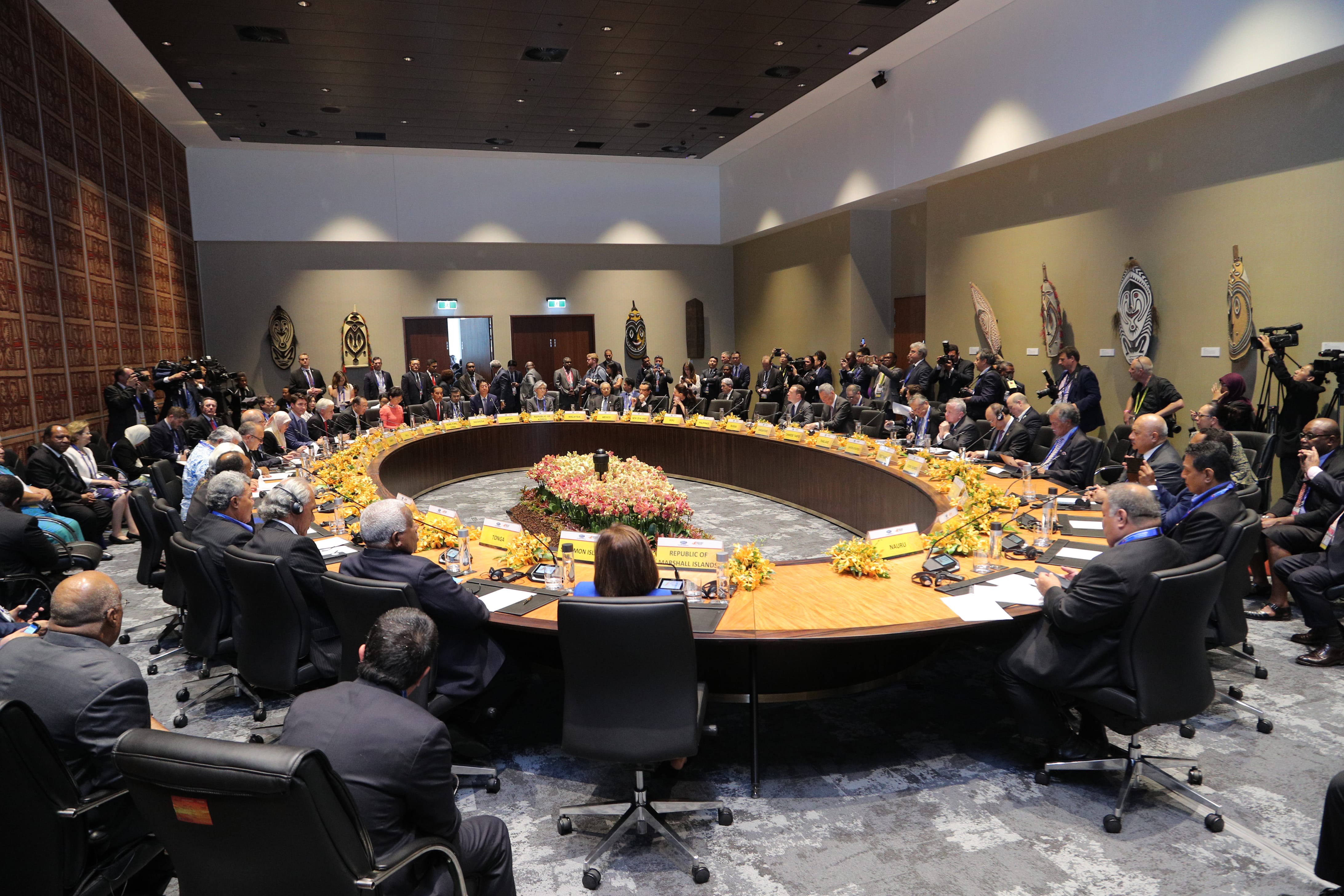 Large round table with seated politicians and journalists in a conference room.