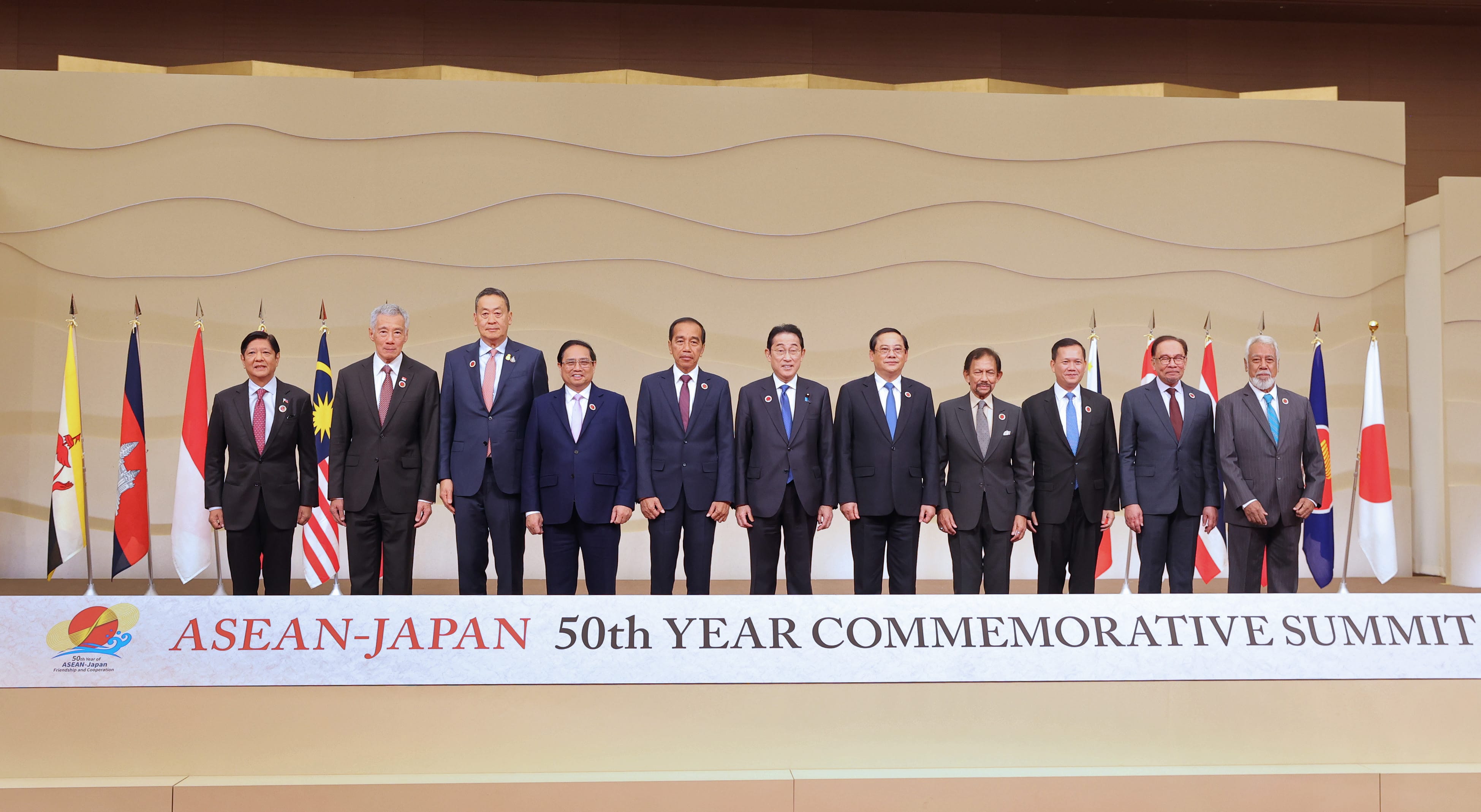 Leaders in suits stand before flags for ASEAN-Japan 50th Year Commemorative Summit.