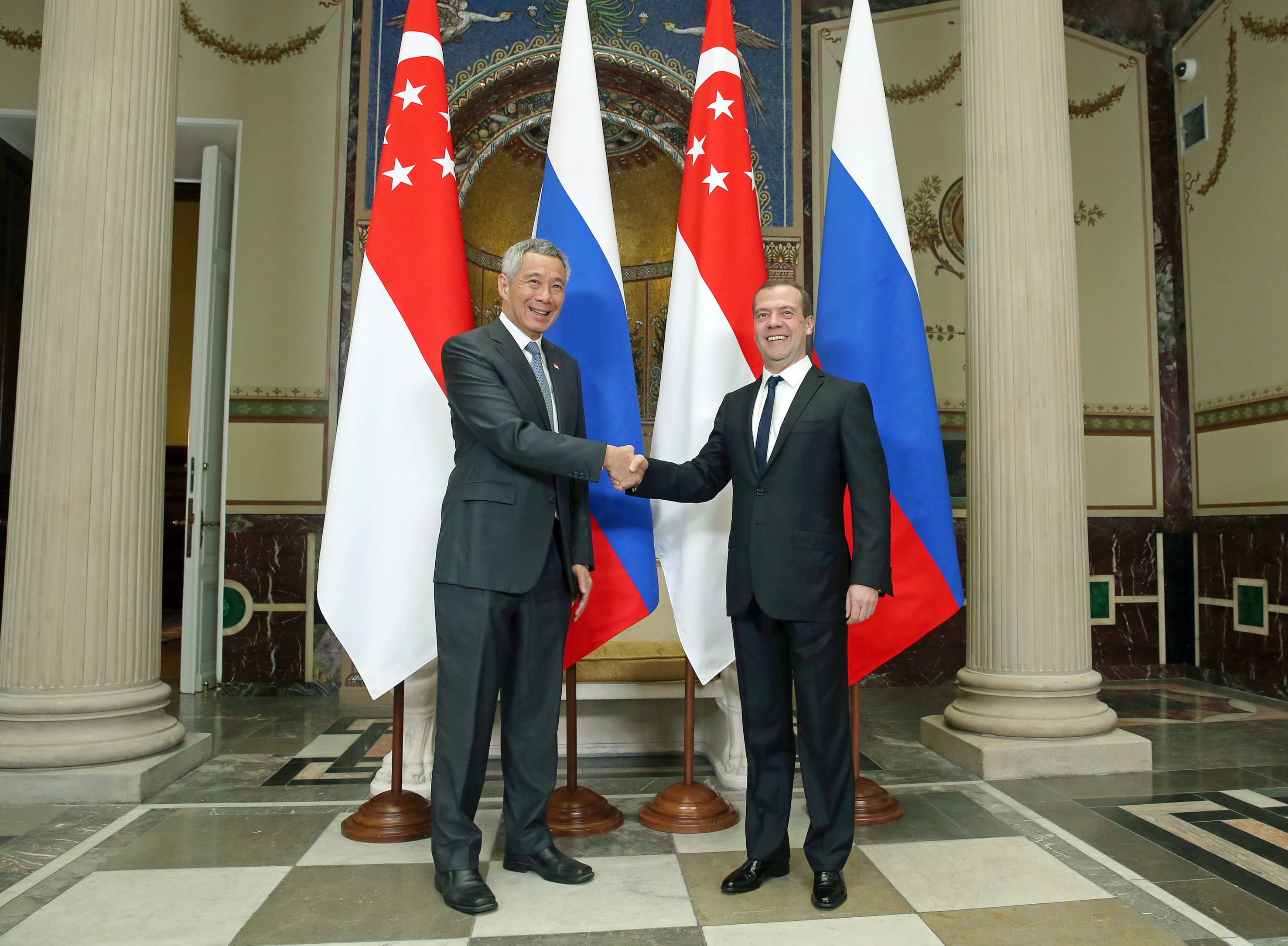 Lee Hsien Loong and Dmitry Medvedev shake hands before Singaporean and Russian flags.