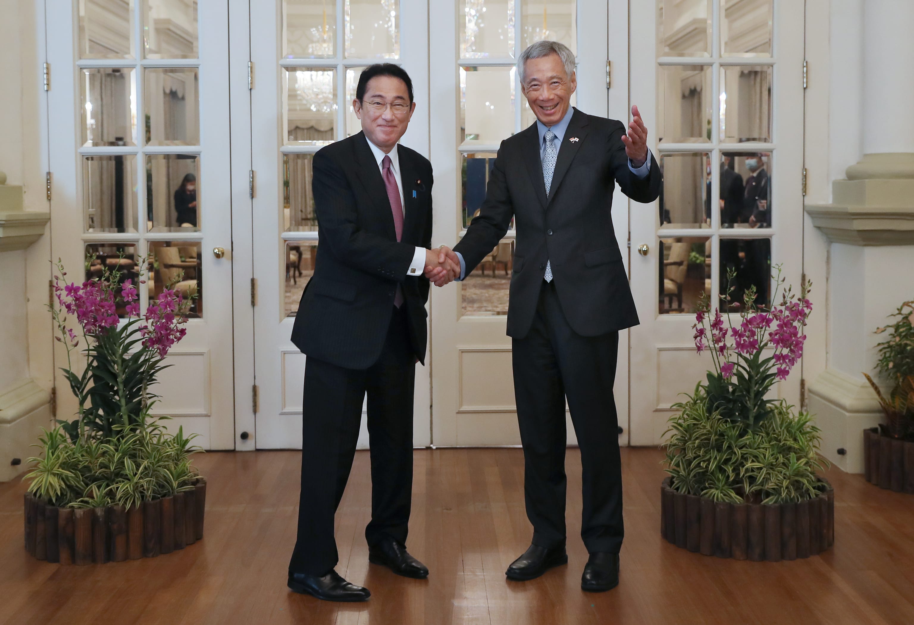 Lee Hsien Loong and Fumio Kishida in suits shake hands in front of glass doors.
