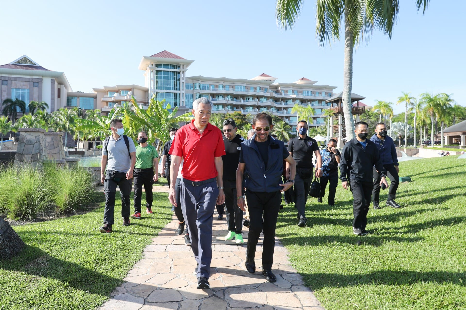 Lee Hsien Loong & Sultan of Brunei walk with entourage on stone path in front of building.