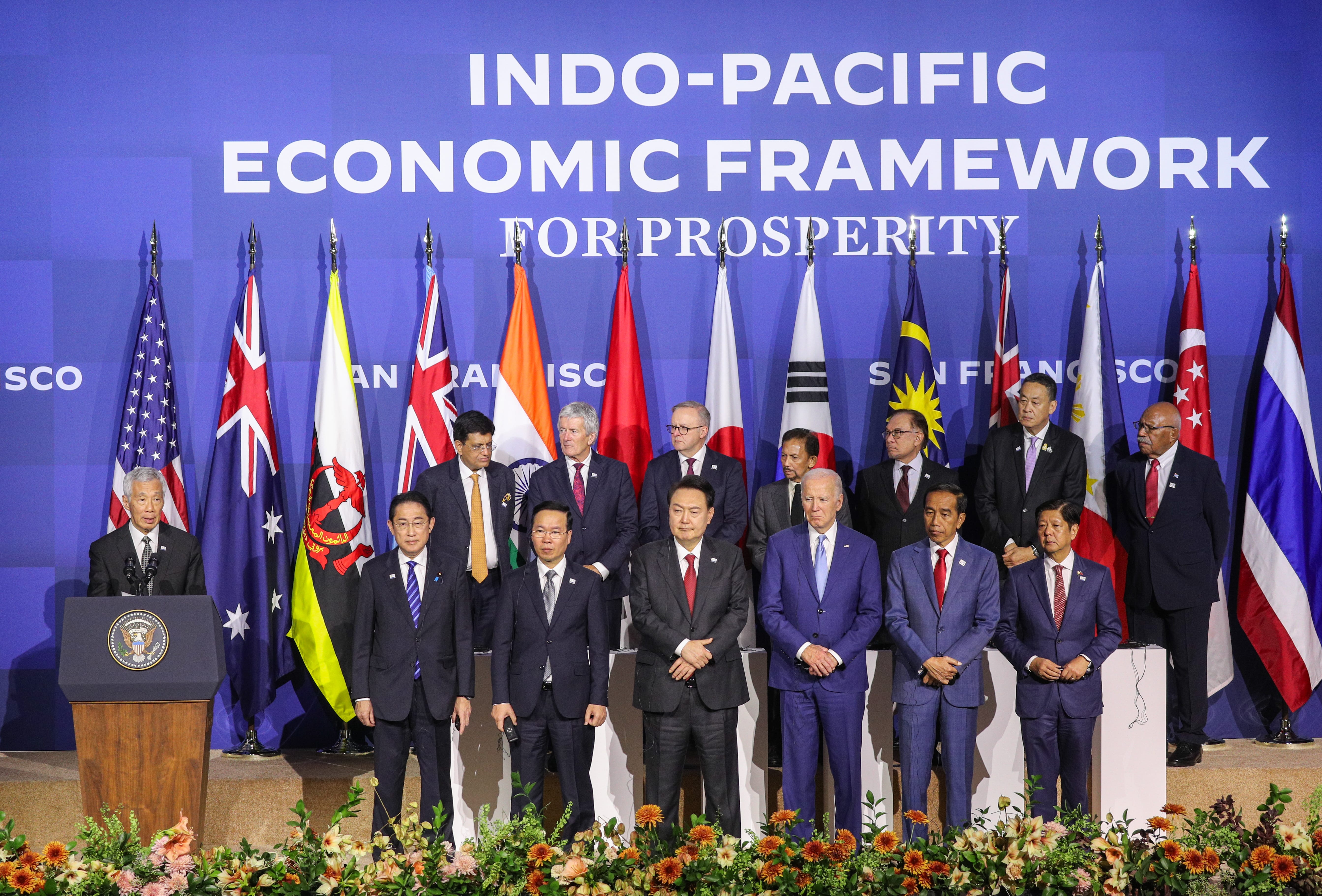 Group of world leaders stand before flags, banner reads "Indo-Pacific Economic Framework for Prosperity." Biden visible.