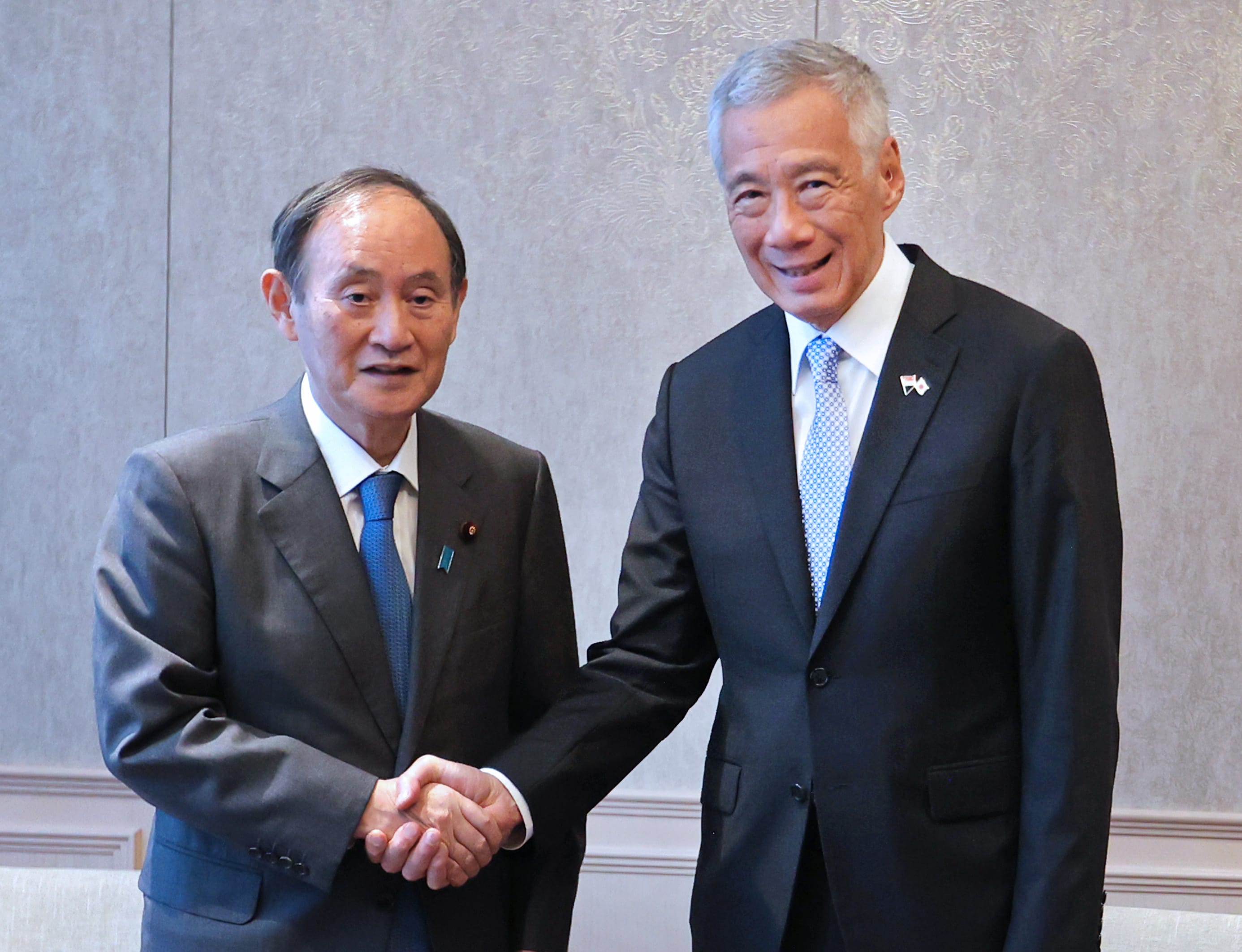 Yoshihide Suga and Lee Hsien Loong in suits shake hands indoors.