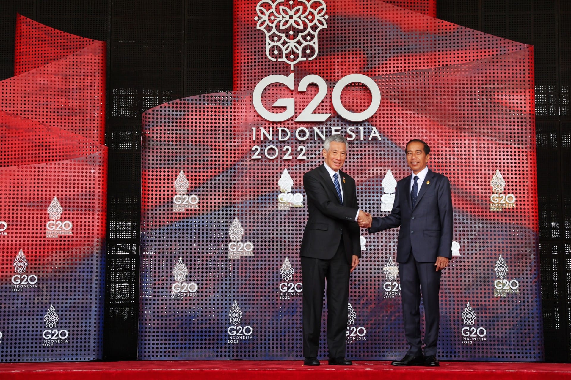 Two men in suits shaking hands, G20 Indonesia 2022 logo in background.
