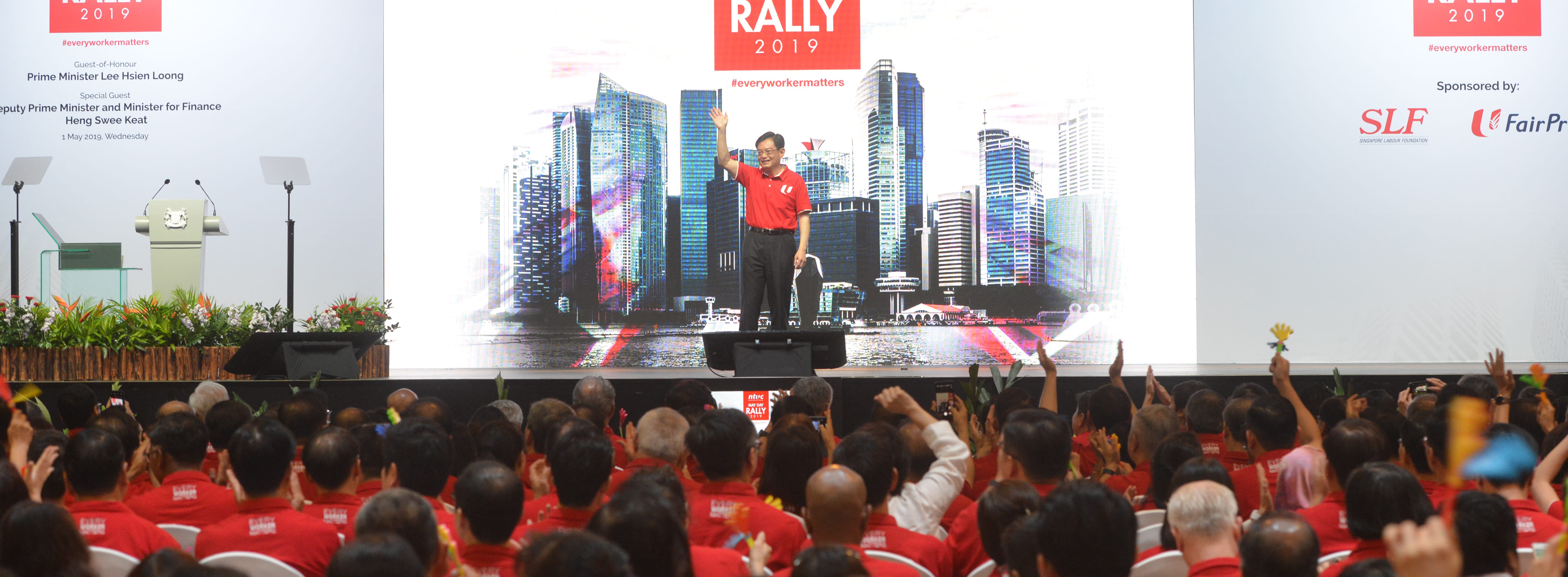 Lee Hsien Loong on stage at NTUC May Day Rally 2019, audience visible. SLF & FairPrice logos.
