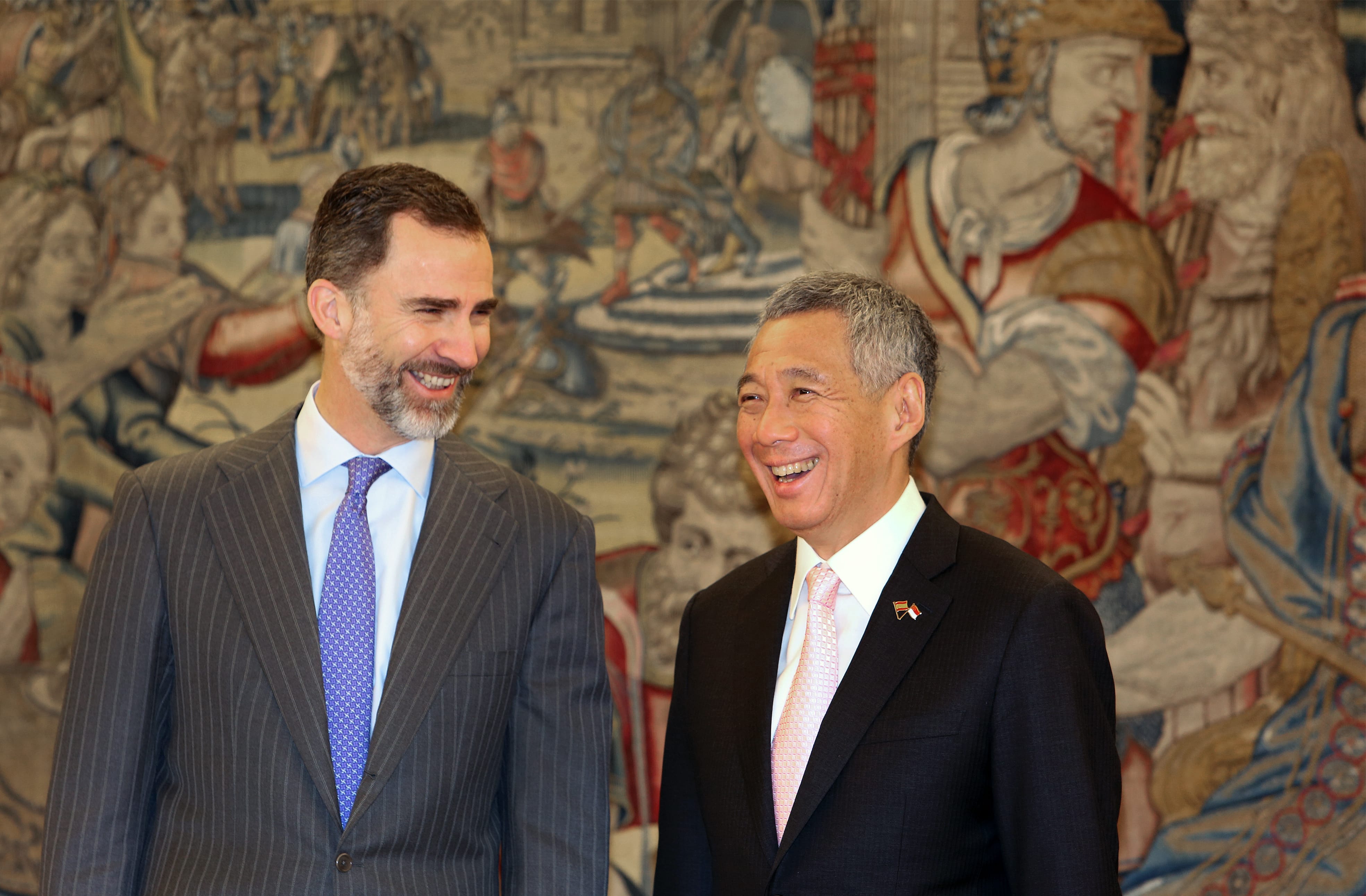 King Felipe VI and Lee Hsien Loong in suits, smiling, before a tapestry.