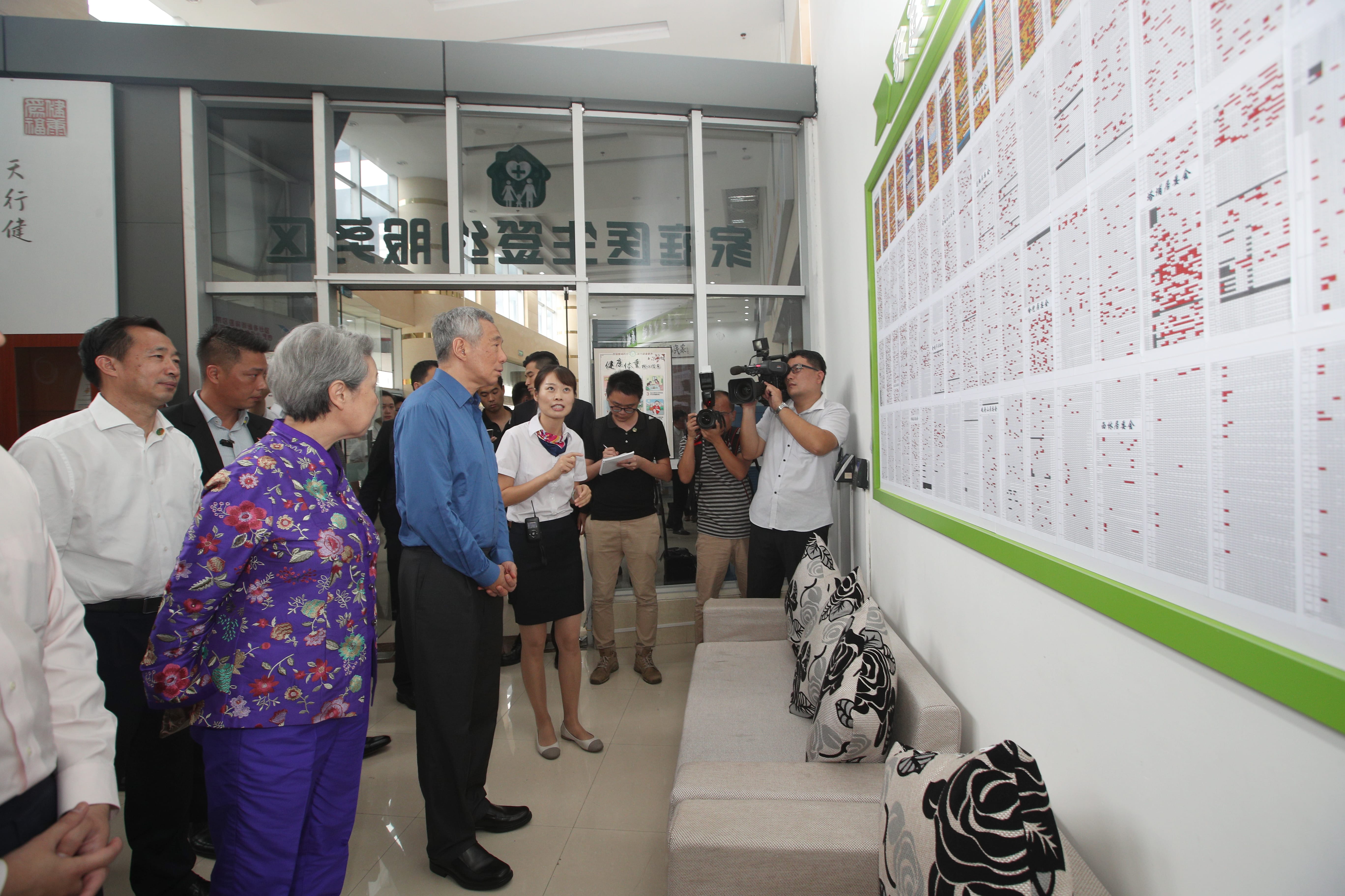 Lee Hsien Loong with staff and press, standing by a large chart-filled wall.