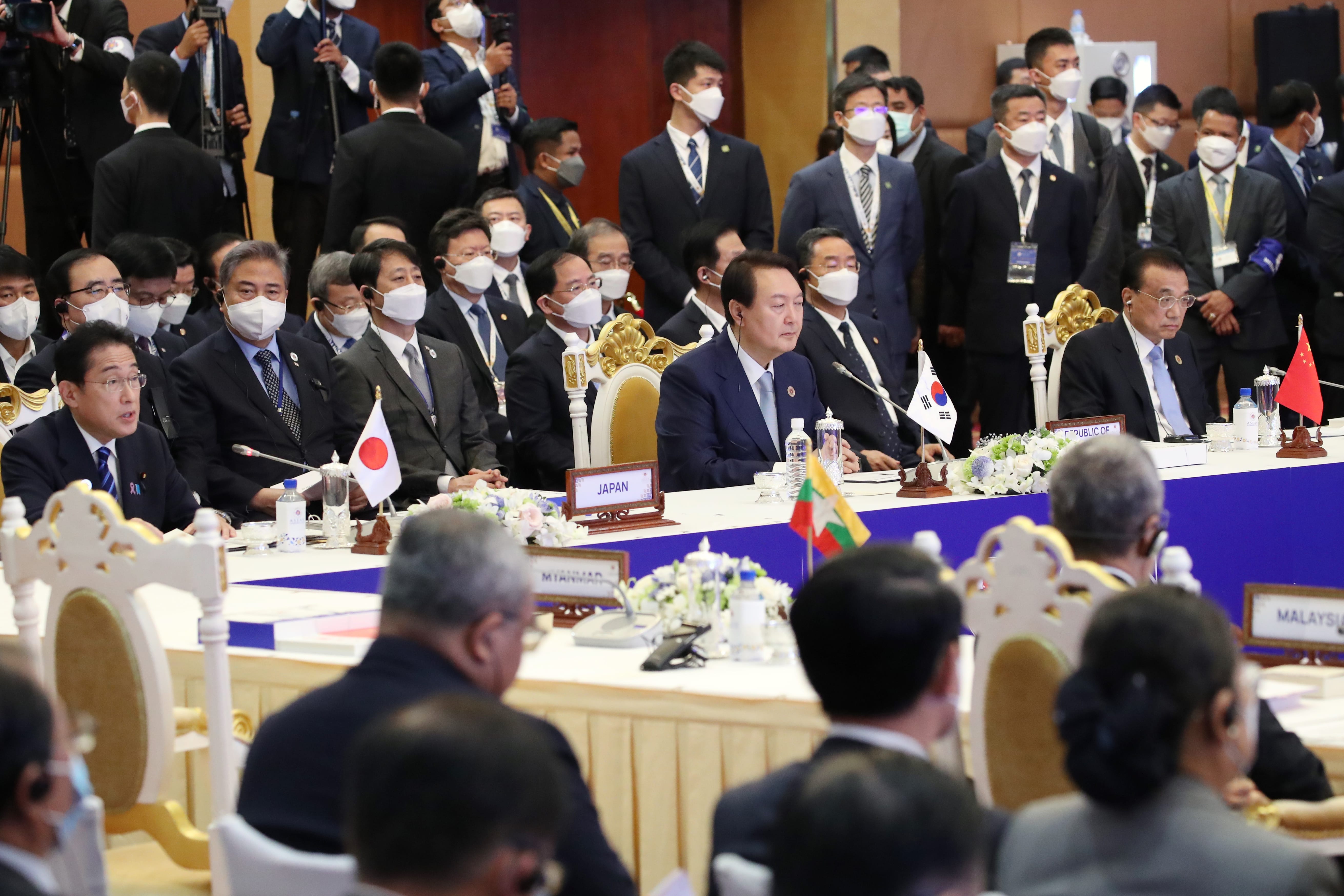 International conference with dignitaries at tables and people observing. National flags visible.