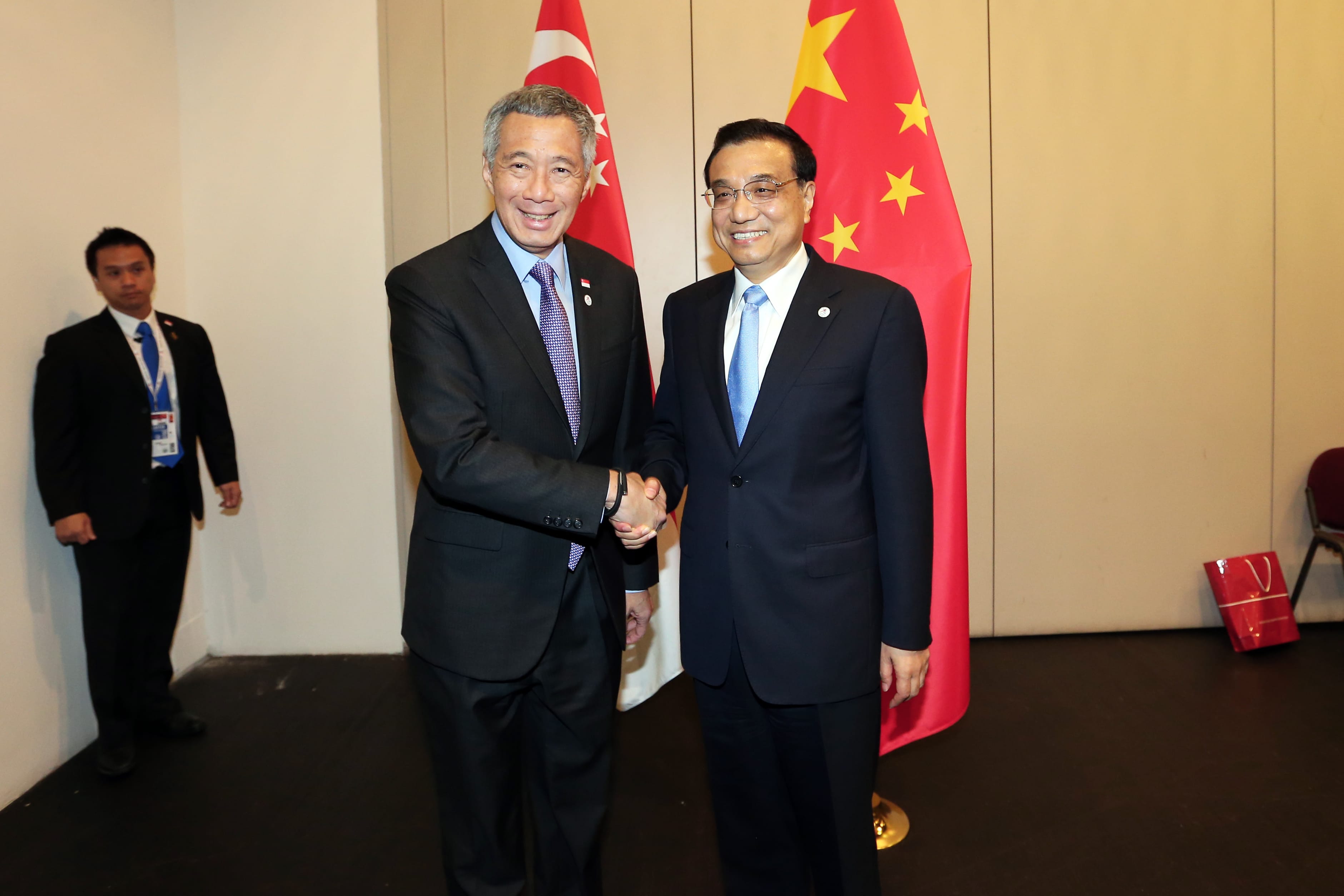 Two men in suits shaking hands between Singapore and China flags. Man visible on left.