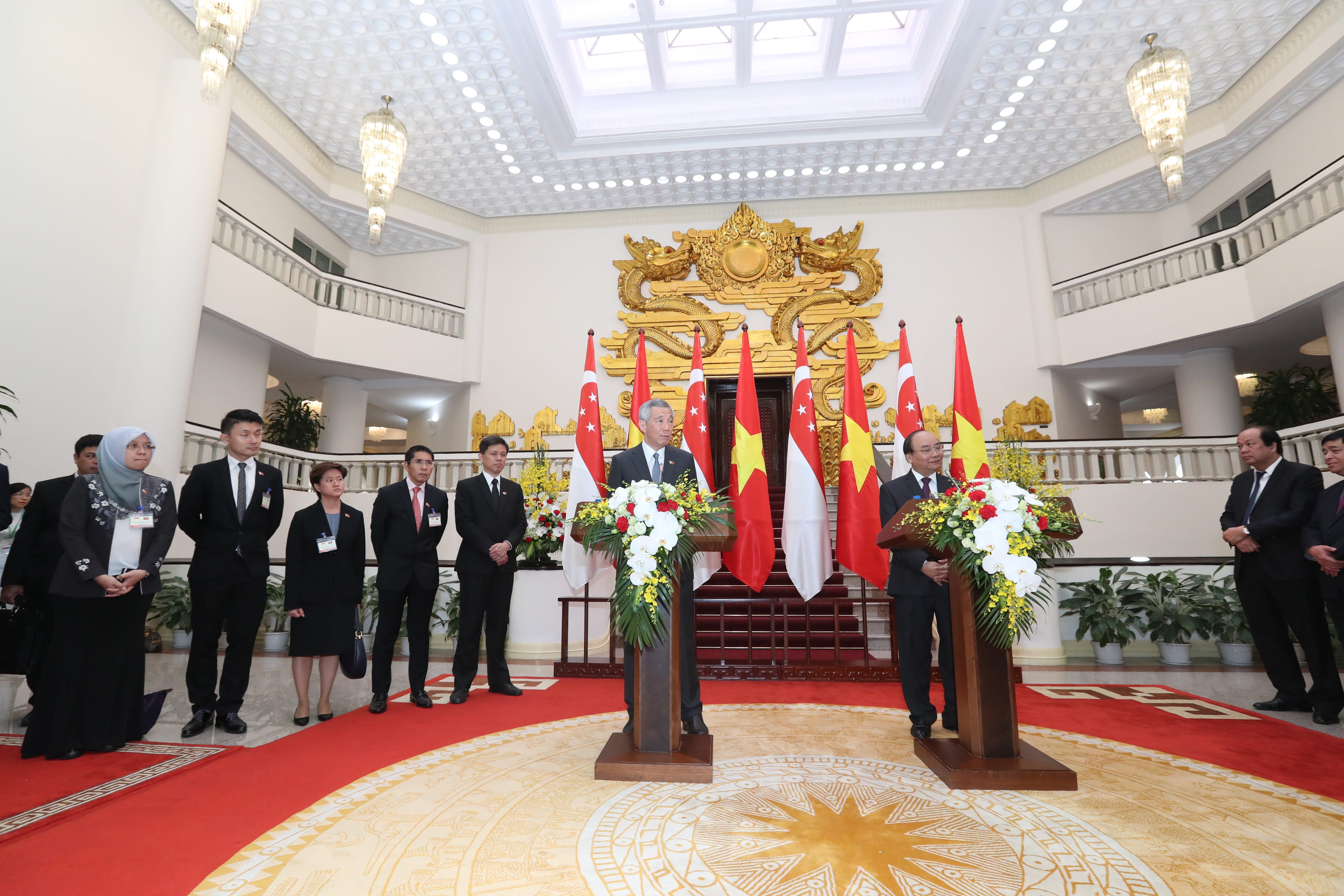 Two men at podiums, Lee Hsien Loong of Singapore, Vietnam flags, ornate hall.