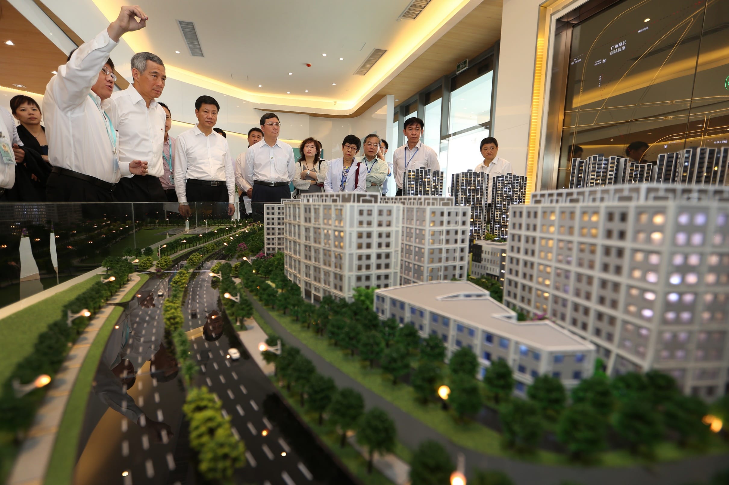 Group of people viewing scale model of city buildings with miniature roads and cars.