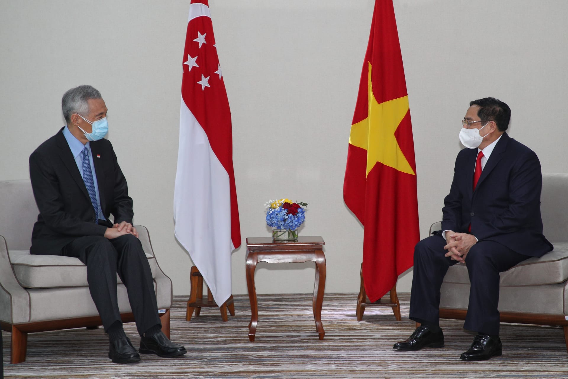 Two masked men in suits seated near Singapore and Vietnam flags.