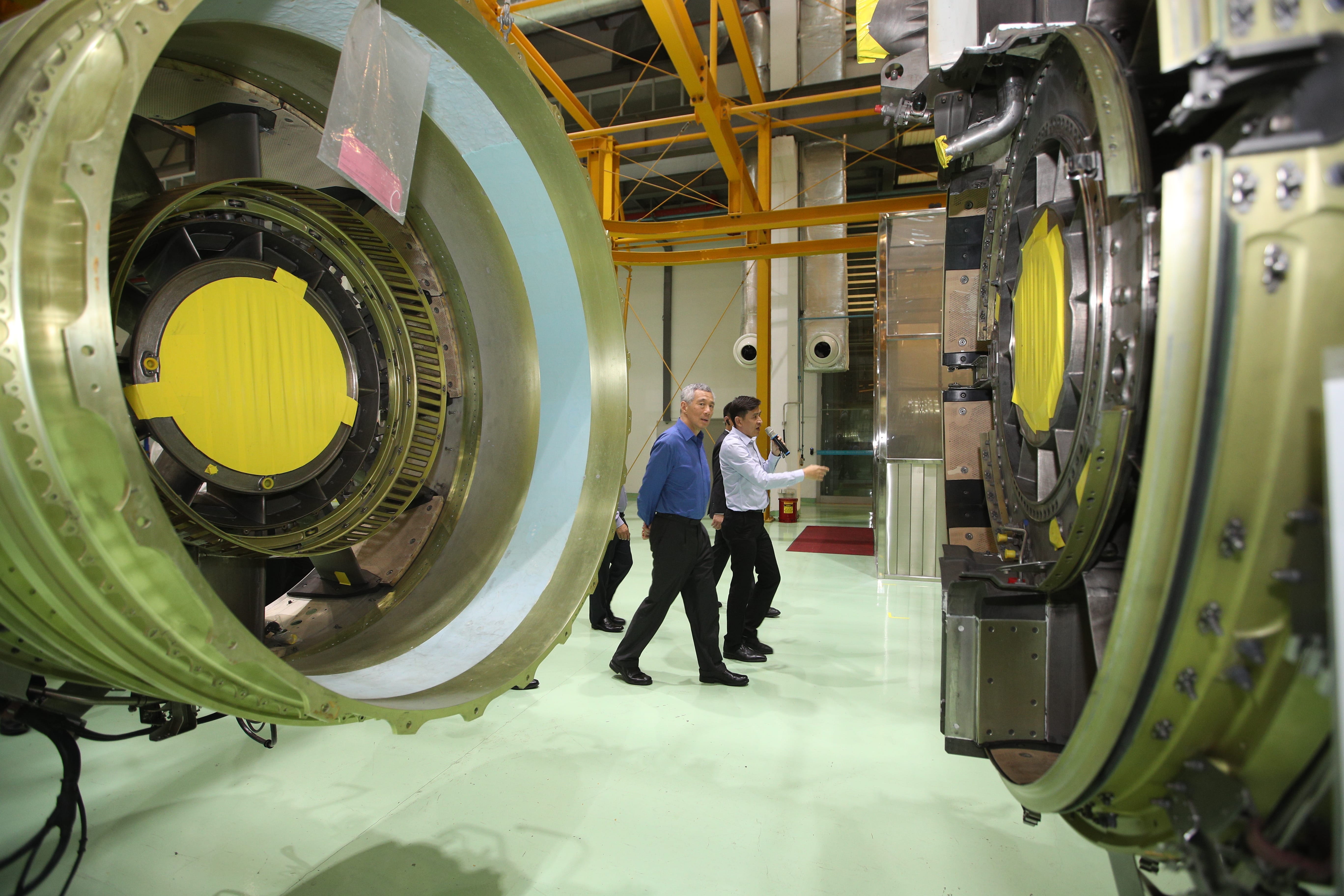 Lee Hsien Loong tours aviation facility, inspecting jet engine components.