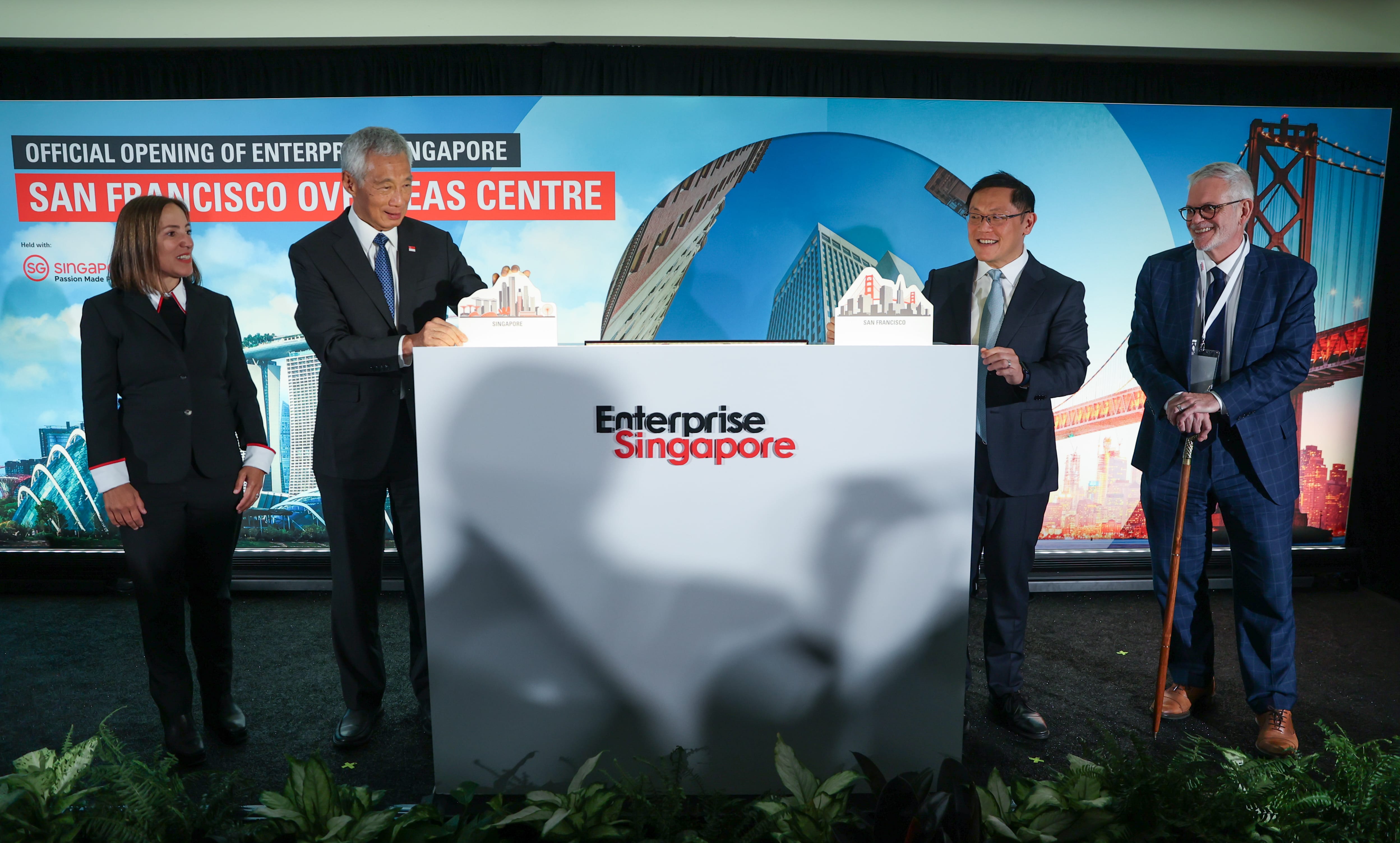 Four people at the "Enterprise Singapore" opening; backdrop displays Singapore and San Francisco skylines.