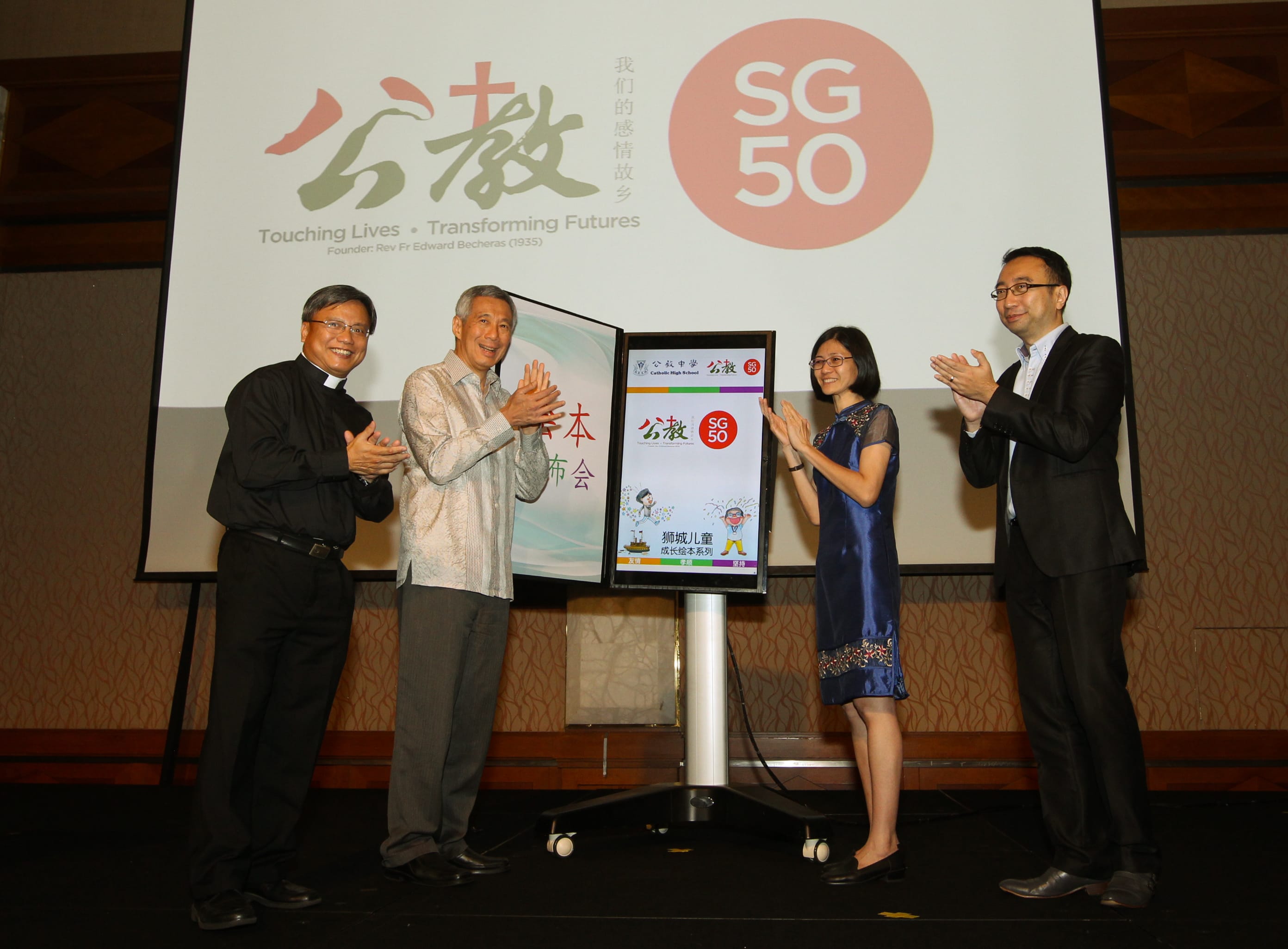 Four people clapping, next to a stand with "Catholic High School" and "SG50" logos.