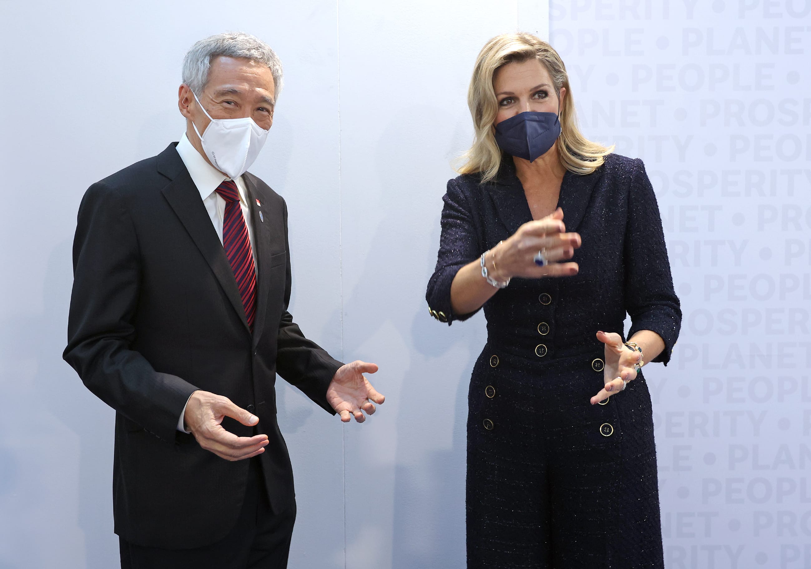 Singapore PM Lee & Queen Maxima, masked, stand gesturing against a wall of text.