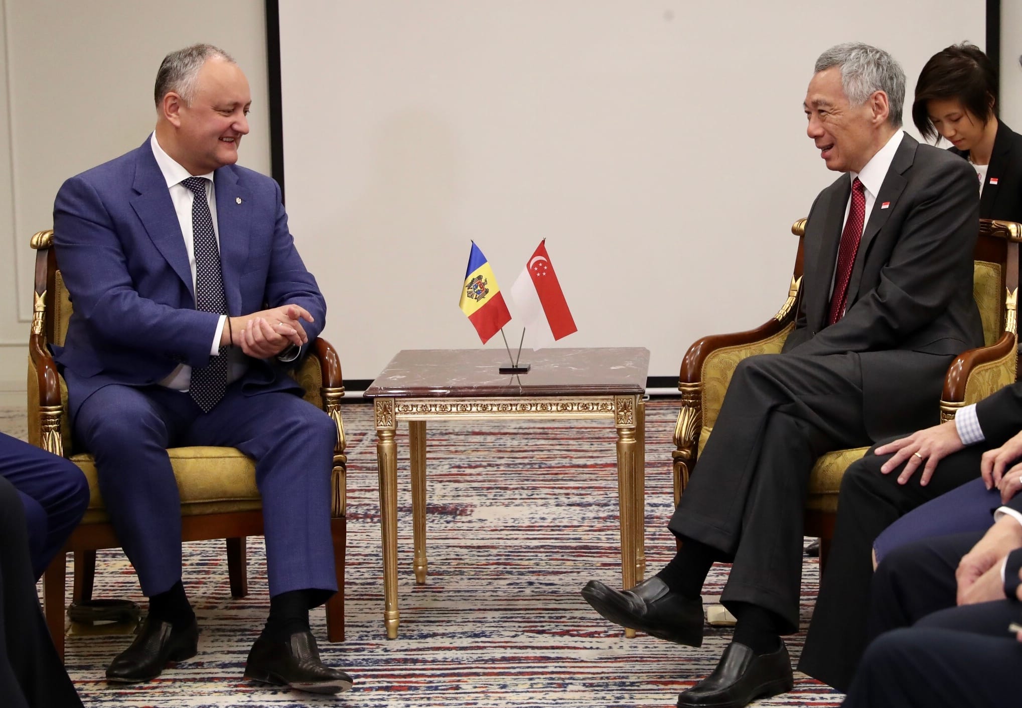 Two men in suits sit facing each other with Moldovan and Singaporean flags on a table.