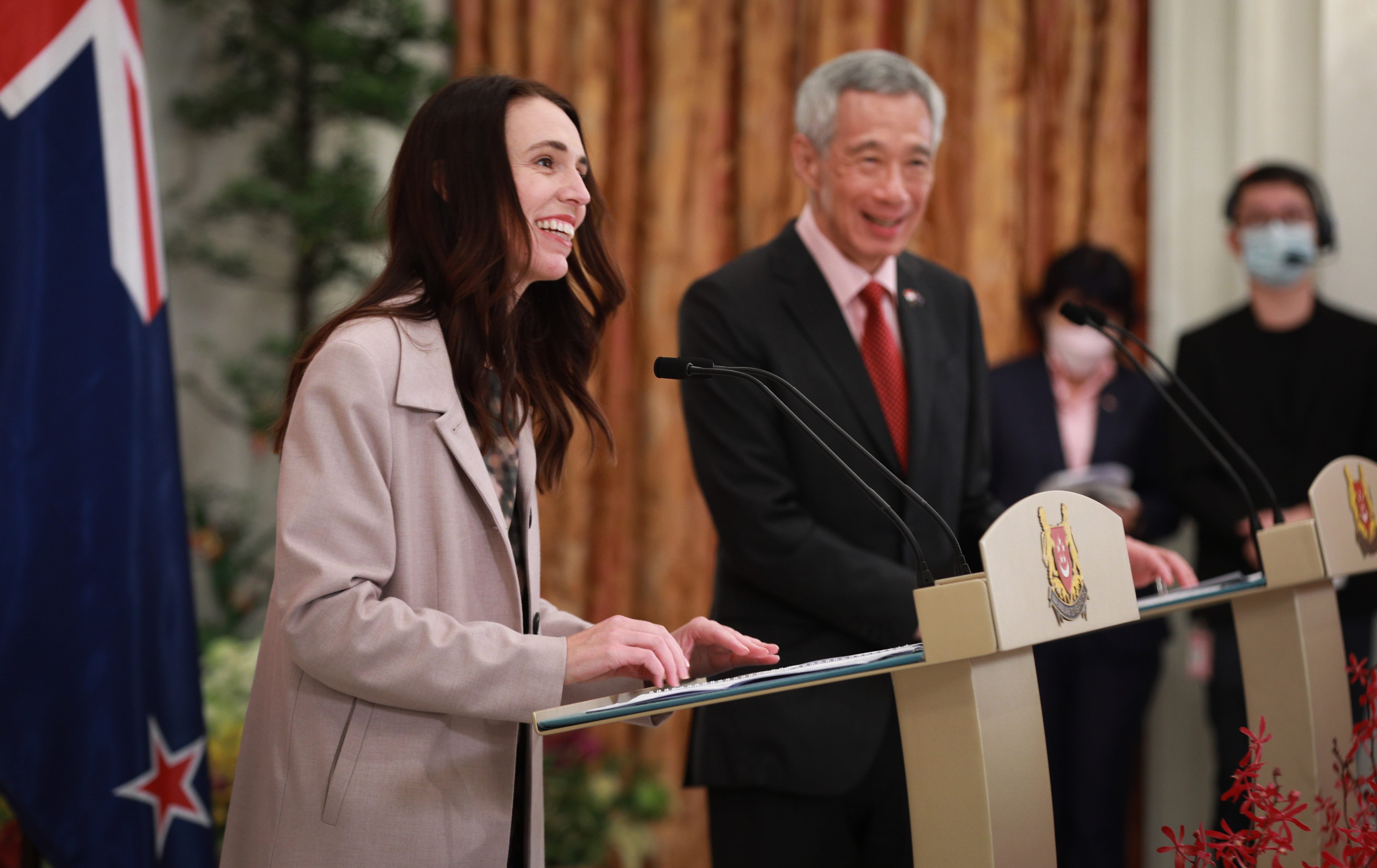 Jacinda Ardern and Lee Hsien Loong at lecterns, flags visible.