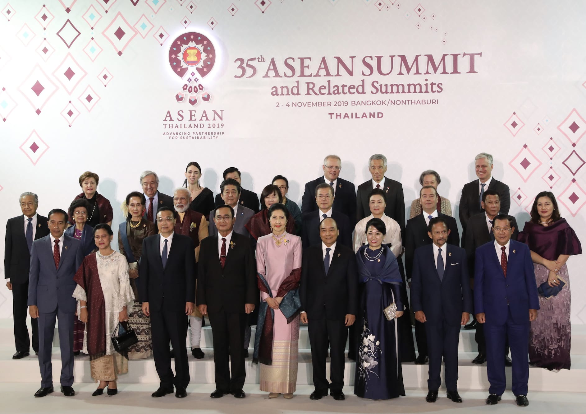 Group posing at 35th ASEAN Summit with logo backdrop. Most are in business attire, some in traditional dress.