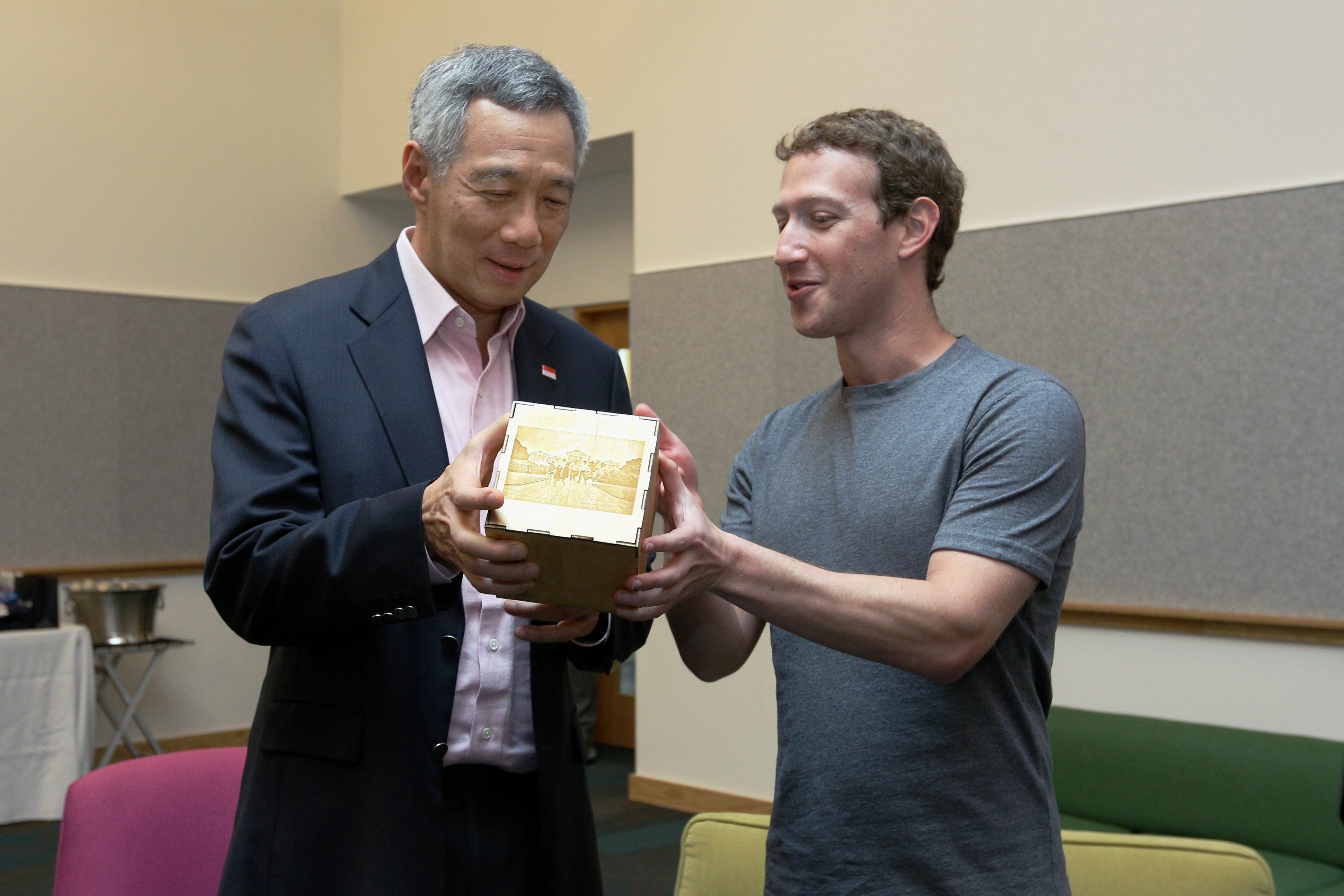 Lee Hsien Loong and Mark Zuckerberg examine a wooden box with an engraved image.