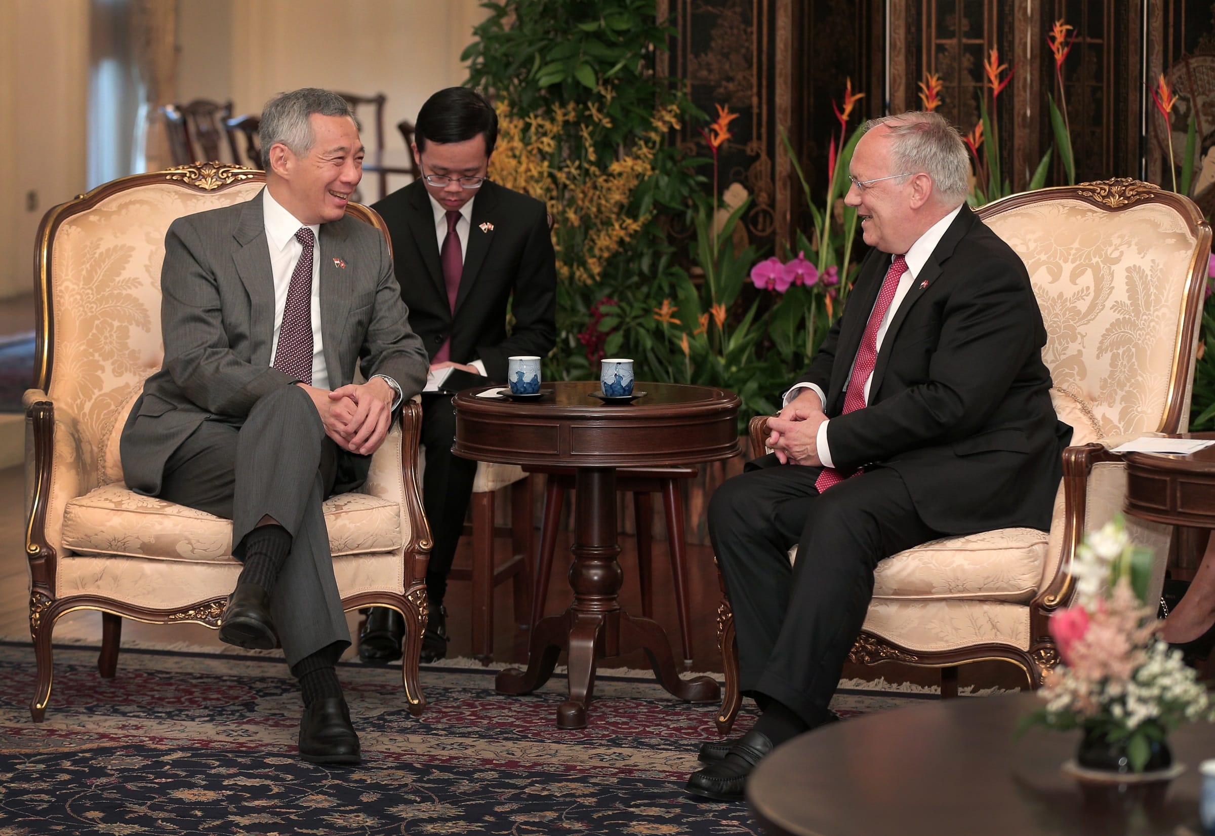 Lee Hsien Loong and man in suits seated on ornate chairs, talking across a small table.