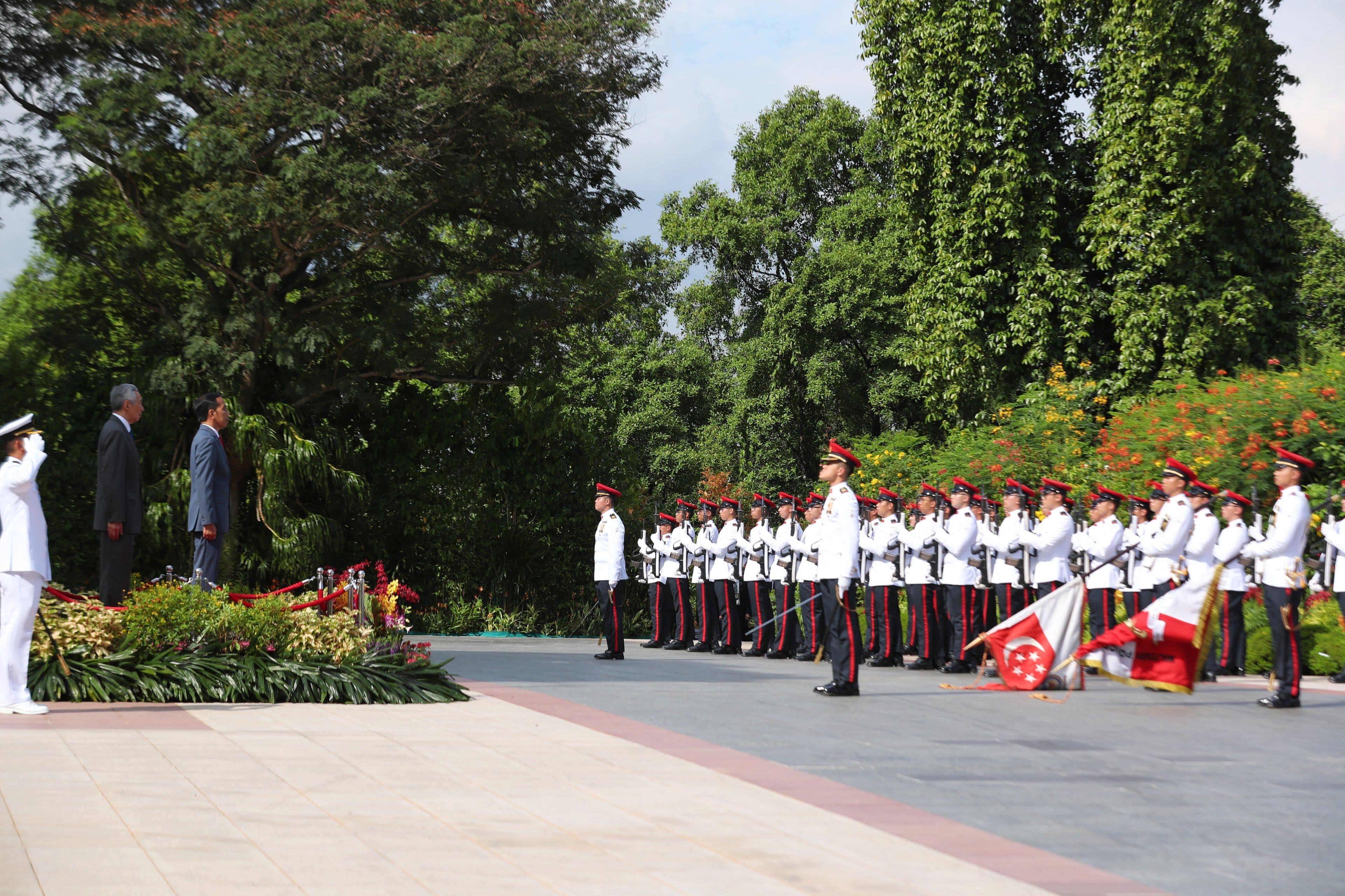 Honor guard with Singapore flag stands at attention for two men in suits.