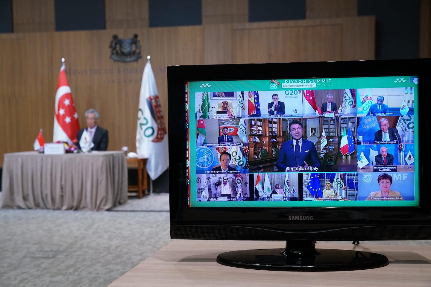 Samsung TV showing G20 Riyadh Summit video call with world leaders. Singapore flag and blurry man visible in background.