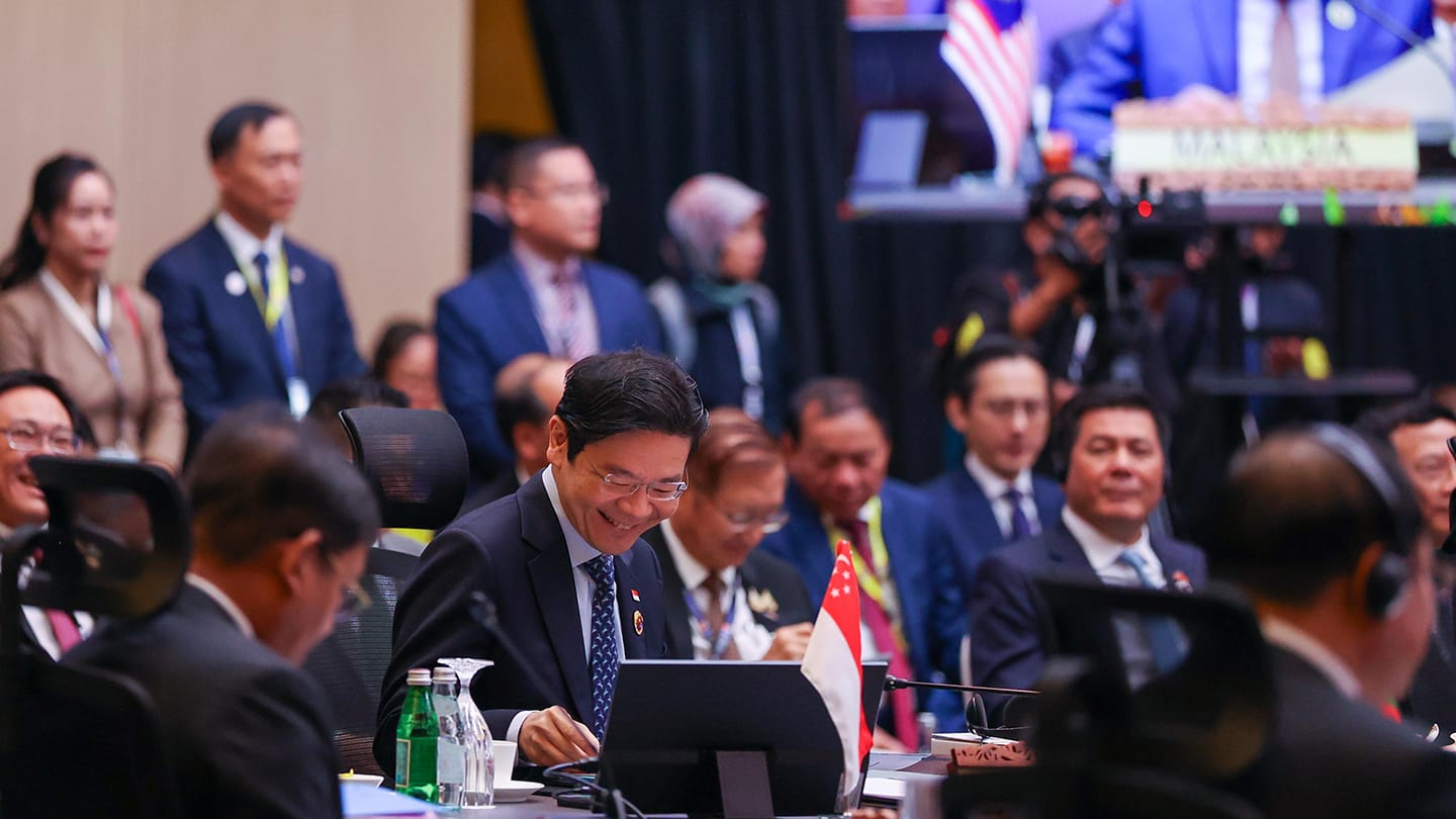Attendees in suits at a conference with Singapore & Malaysia signage visible.