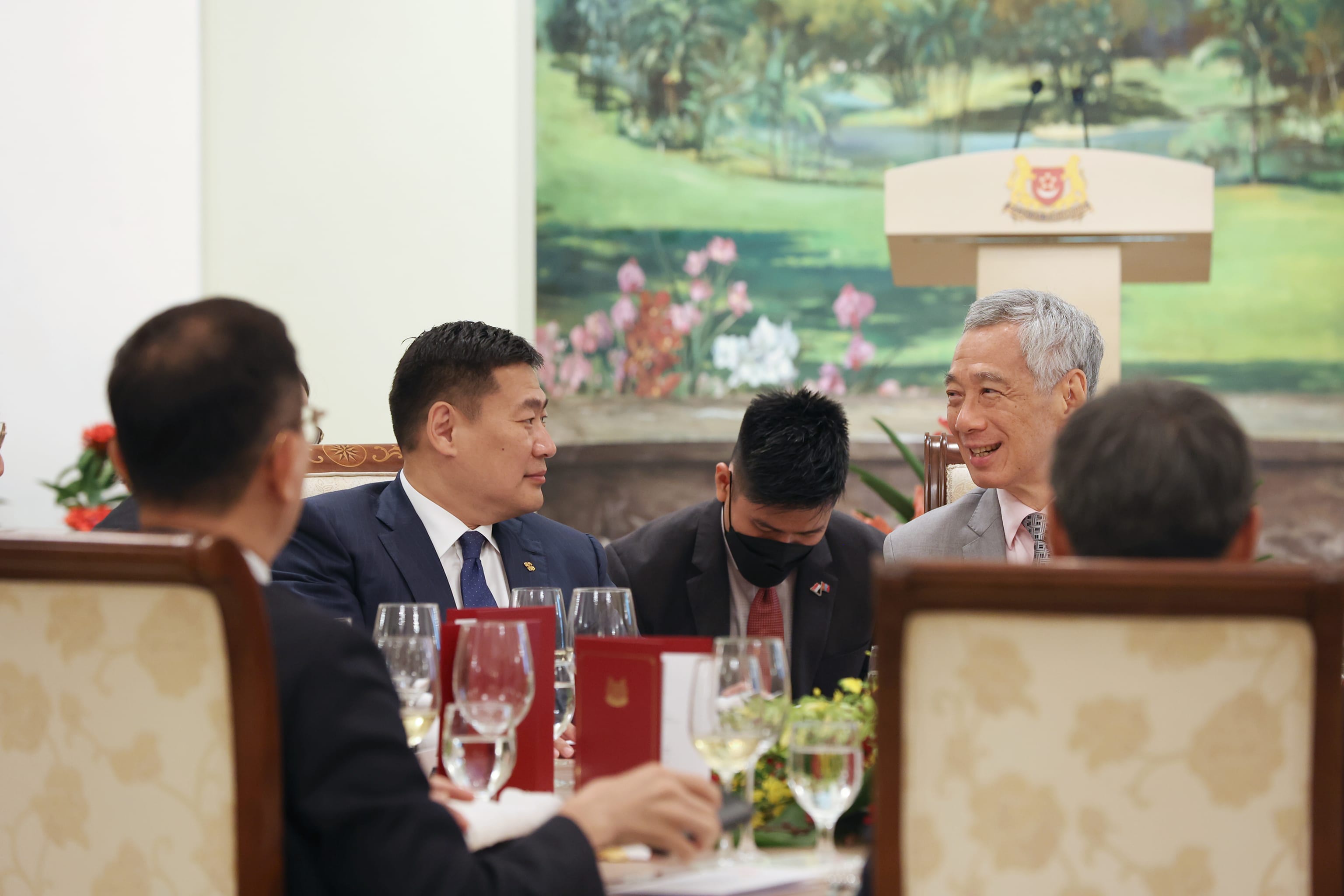 Lee Hsien Loong at a table with others, Singapore coat of arms in background.