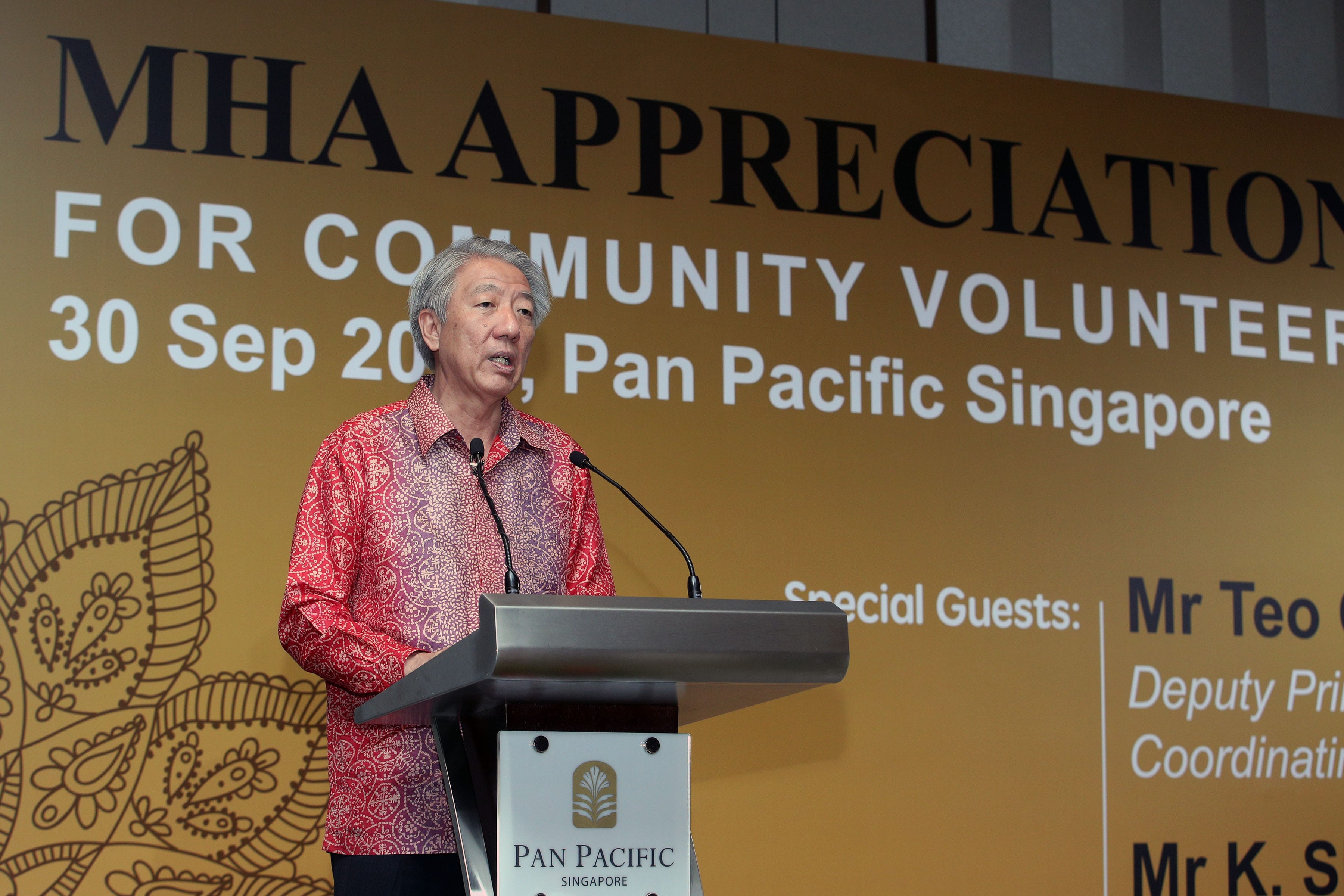 Man in red shirt at Pan Pacific podium with mics. "MHA Appreciation" text backdrop.