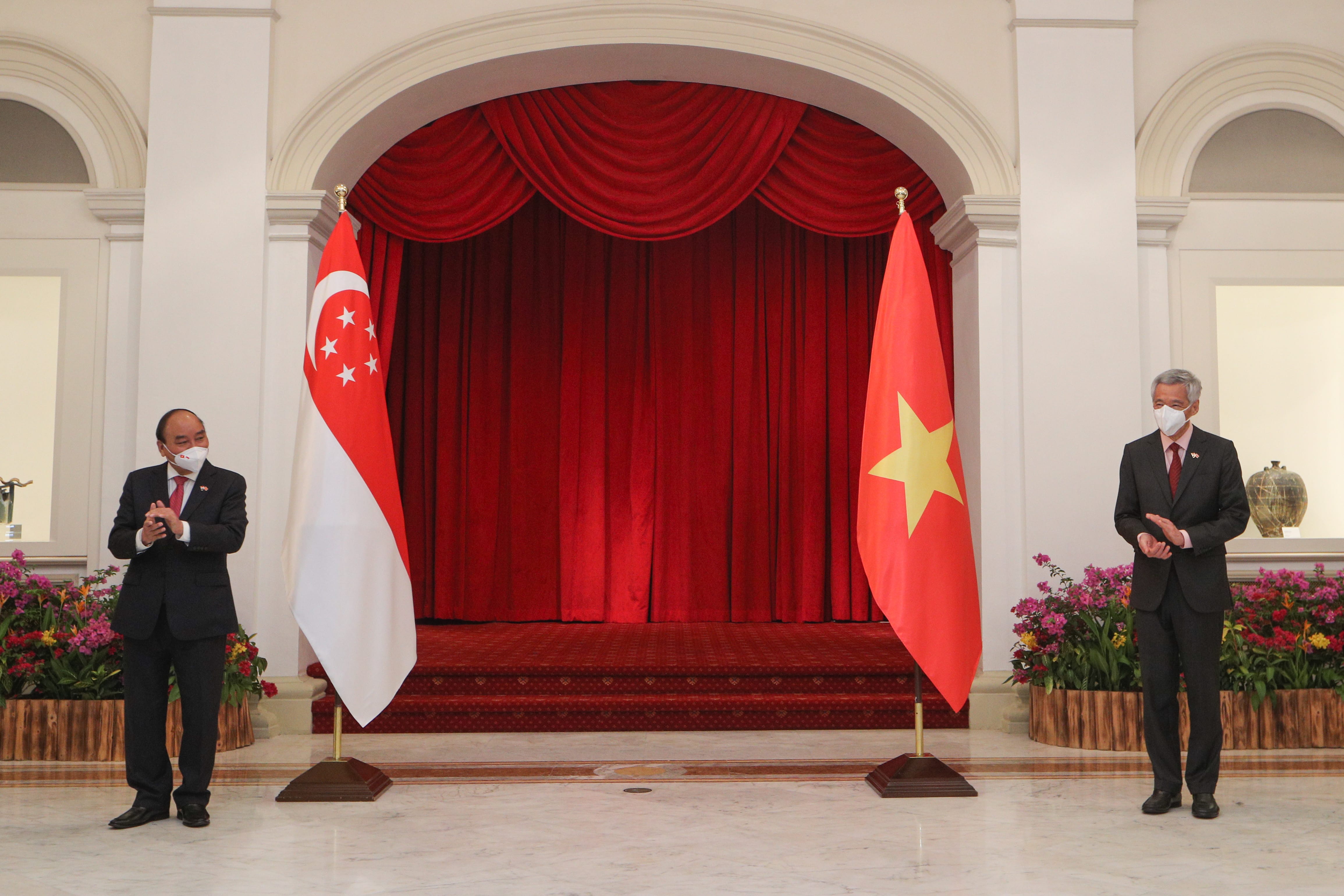 Two men in suits flanking Singapore and Vietnam flags, red backdrop with red curtain.