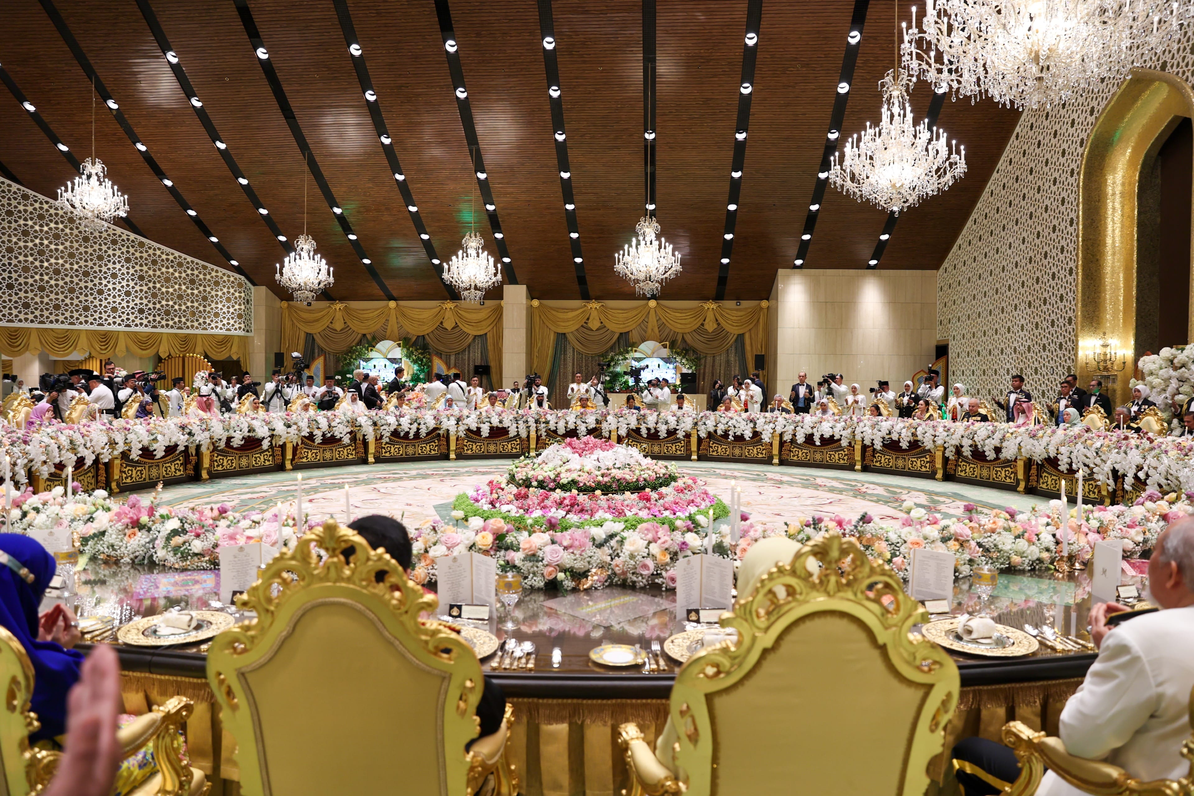 Ornate banquet hall with floral centerpiece, chandelier and people seated at a table.