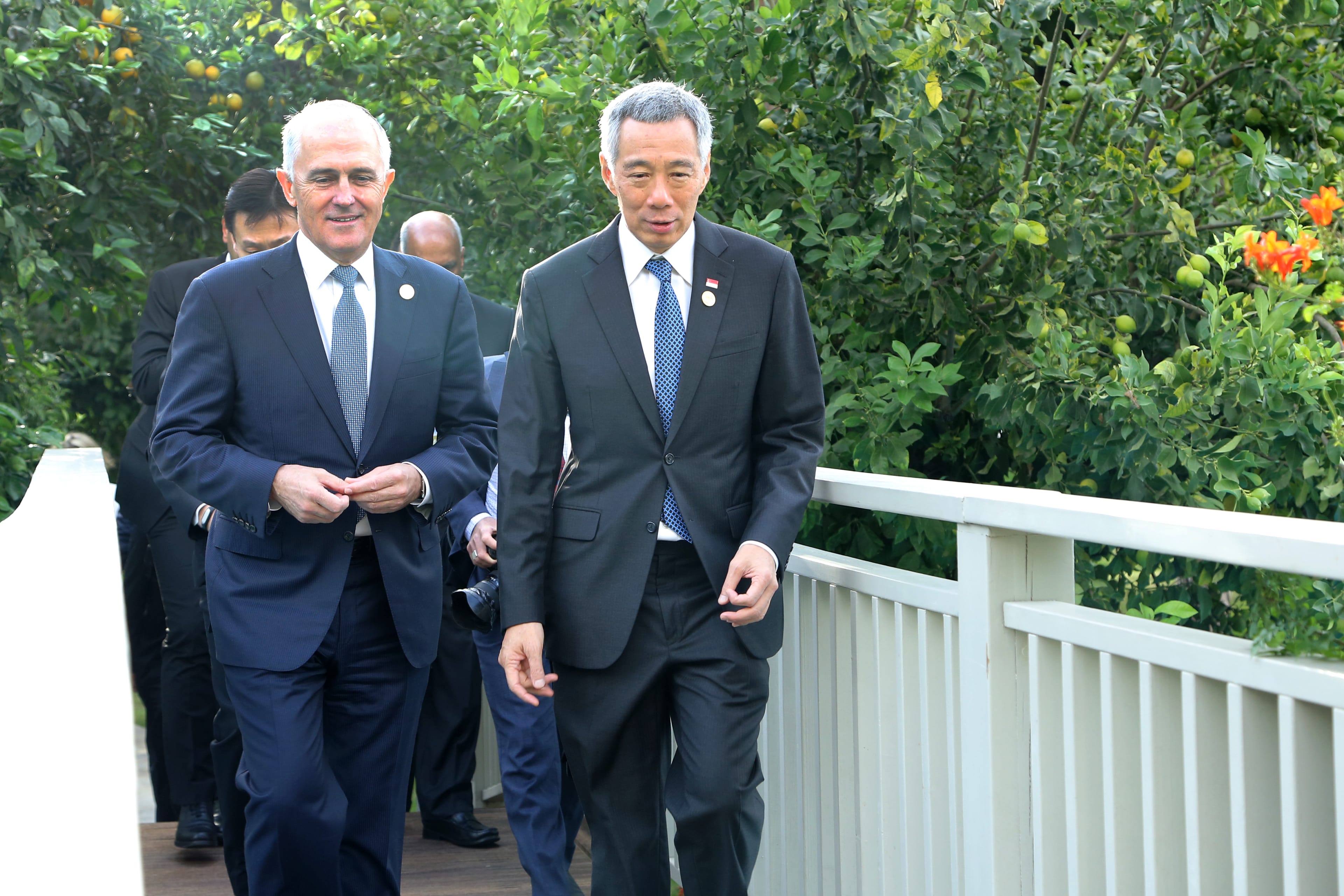 Malcolm Turnbull and Lee Hsien Loong in suits walk across a bridge lined with a white railing.