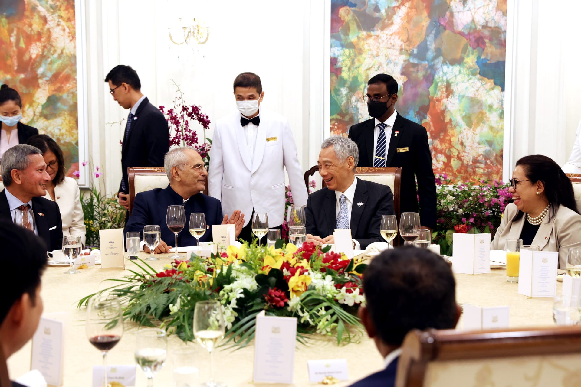 People seated at a formal dining table with waitstaff.