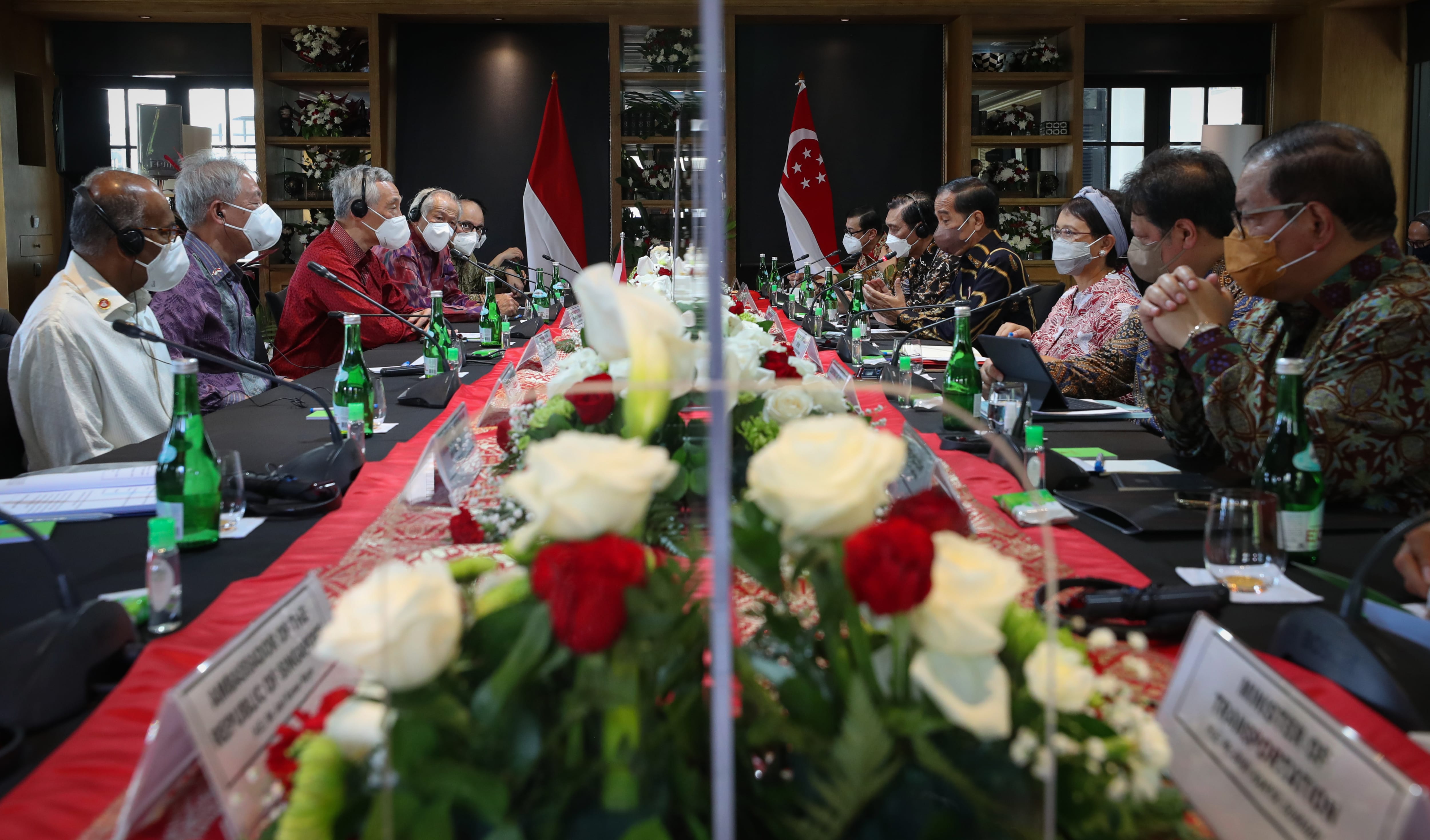 Meeting with Indonesian and Singaporean flags, officials wear masks at a long table.