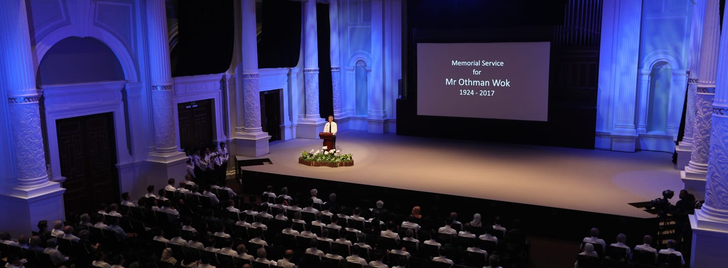 Audience at memorial service for Mr. Othman Wok, speaker at podium on stage.