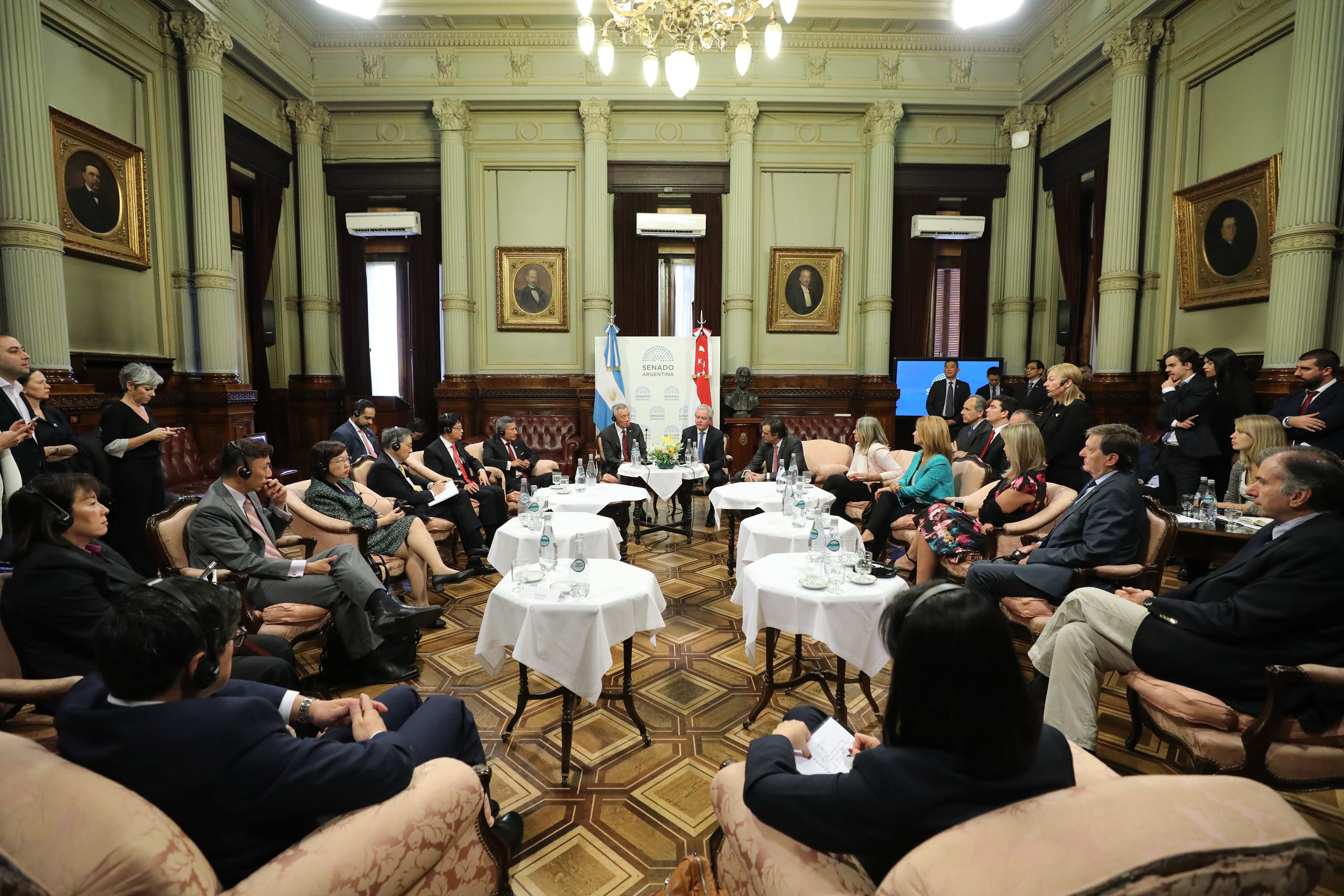 Large group seated in ornate hall; tables with bottled water, SENADO ARGENTINA flags displayed.