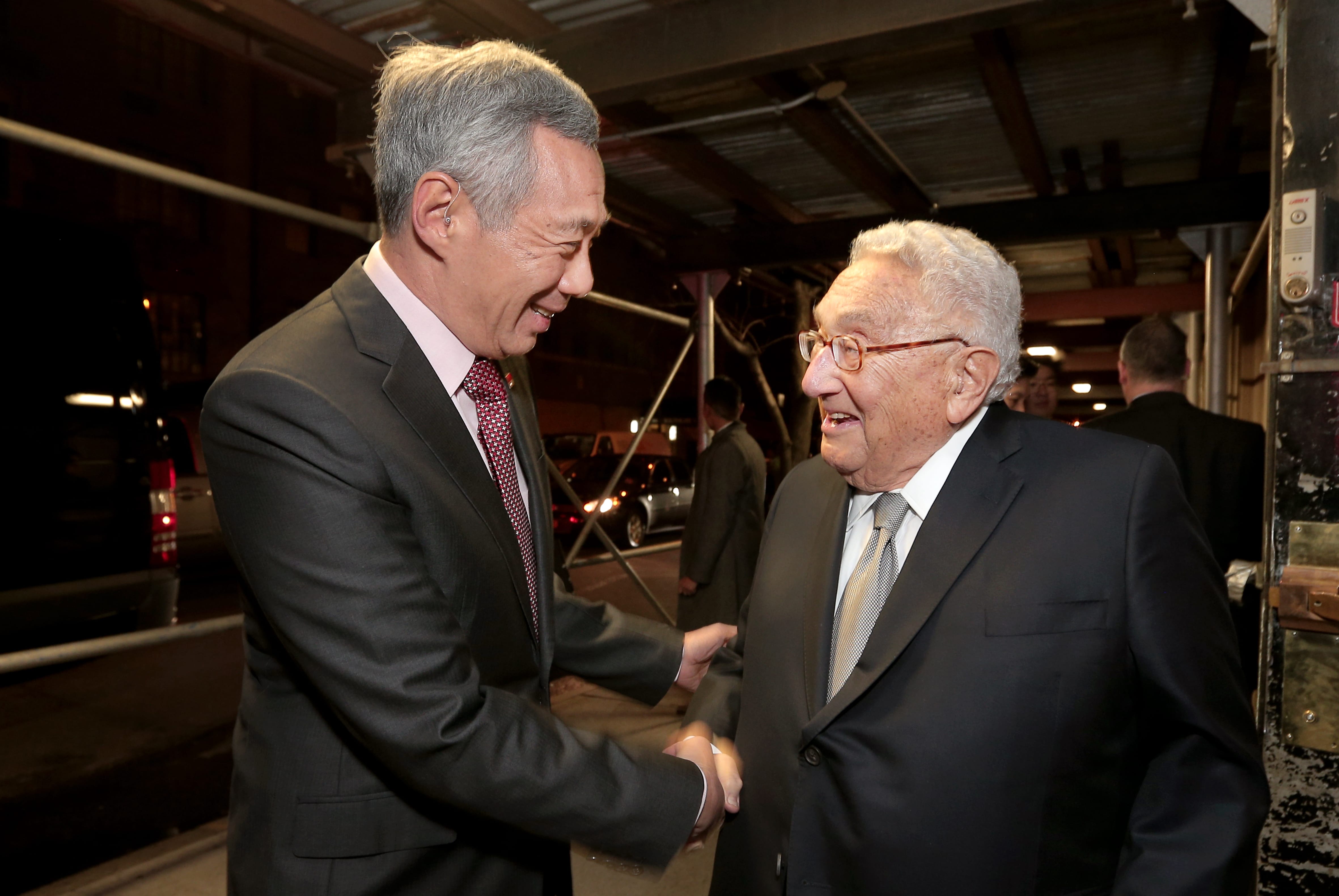 Lee Hsien Loong and Henry Kissinger in suits shaking hands, both smiling.