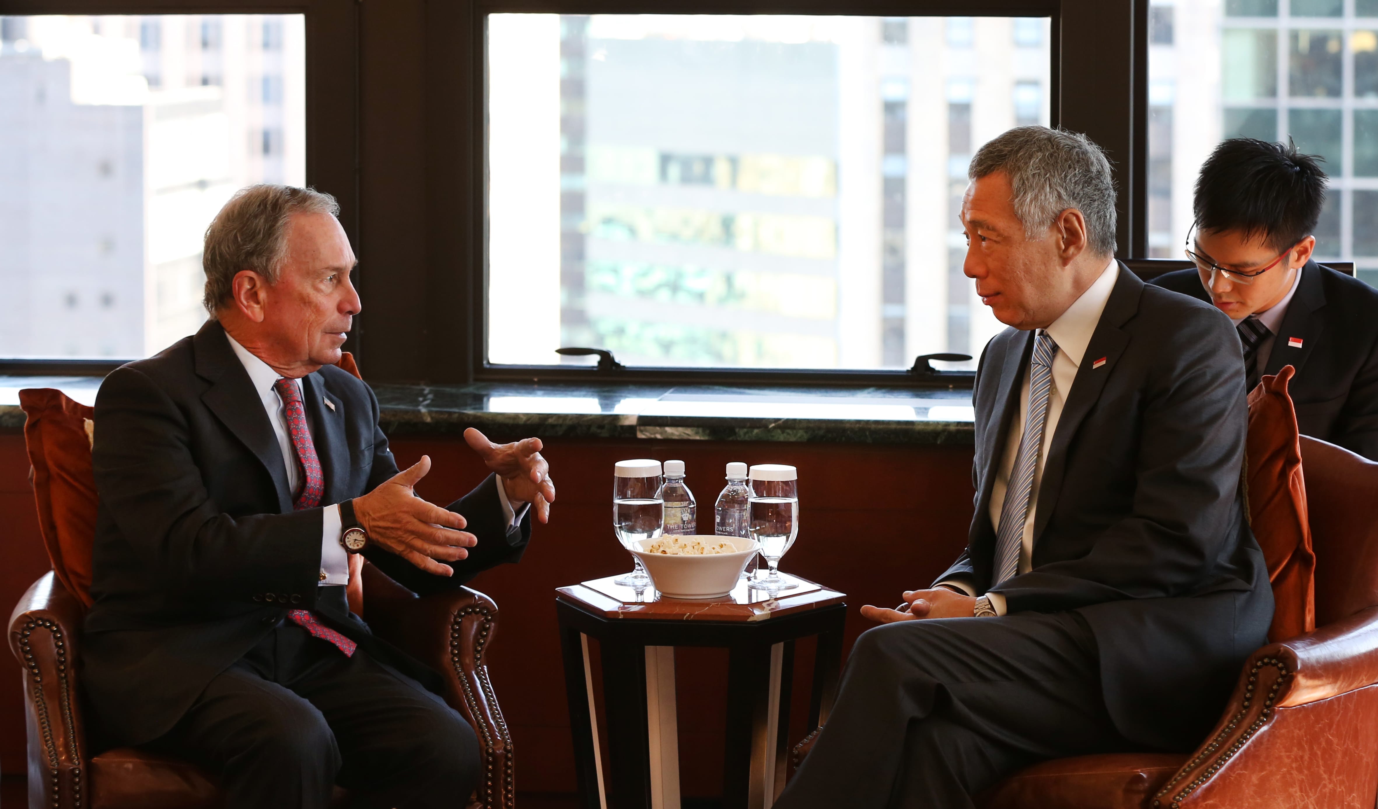 Michael Bloomberg and Lee Hsien Loong in suits facing each other with a window behind them.