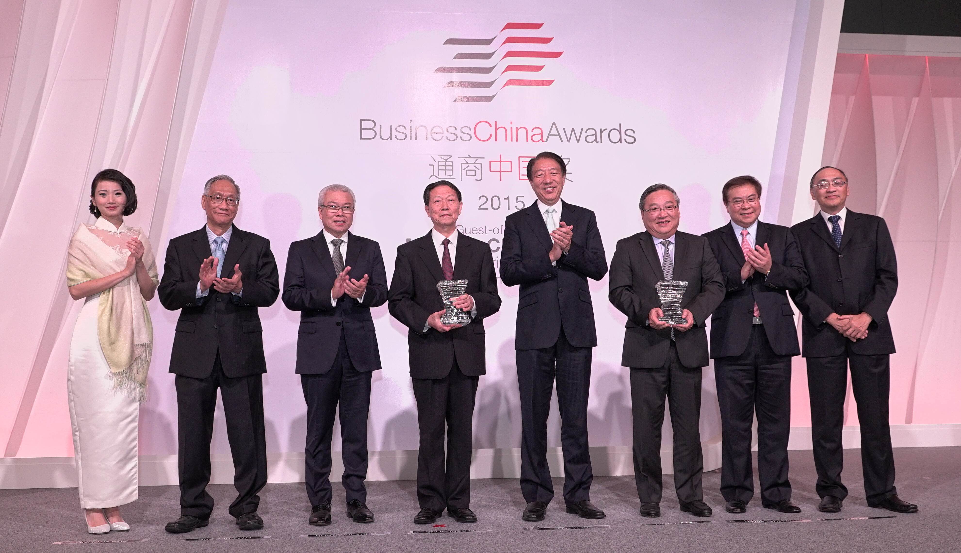 Seven people on stage at the Business China Awards 2015, clapping, some holding awards.