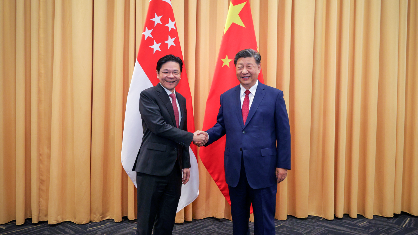Two men in suits shake hands, flanked by Singapore and China flags.