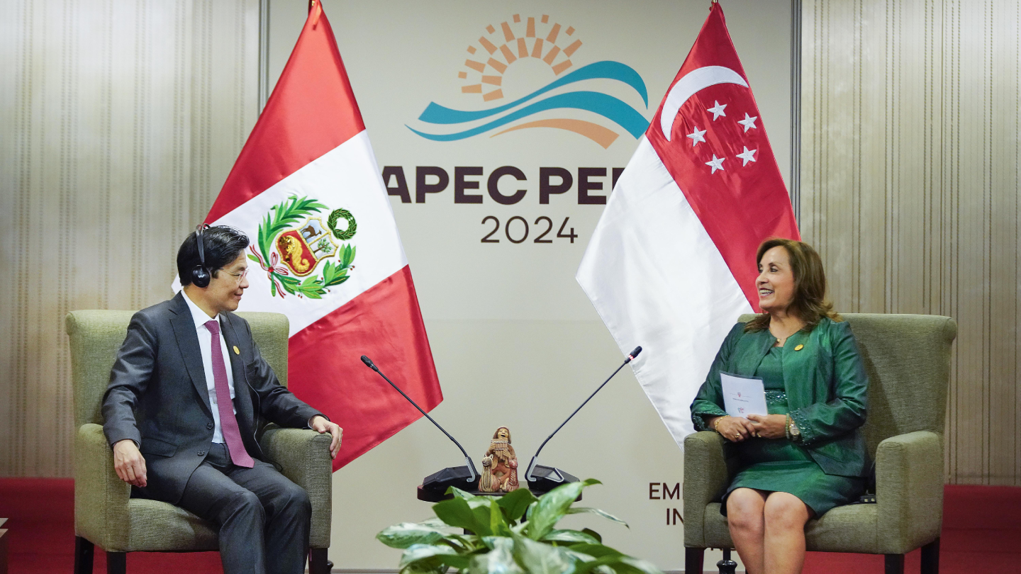 Two people seated before Peru and Singapore flags, APEC Peru 2024 logo on a backdrop.