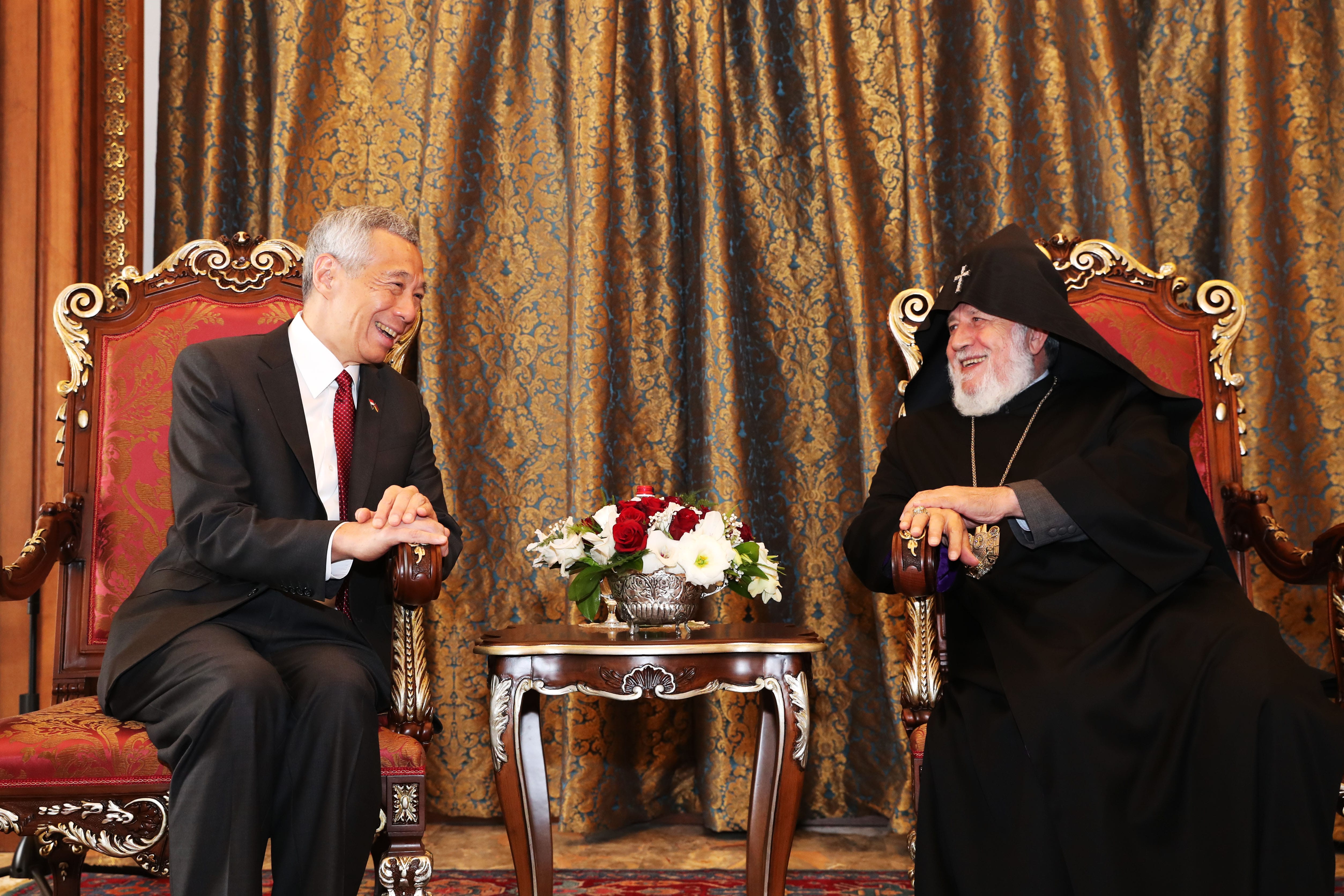 Lee Hsien Loong & religious leader seated on ornate chairs, smiling. Flowers between them.