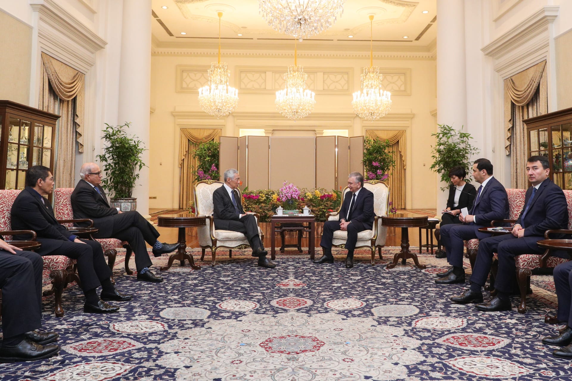 Meeting in ornate room. Two men seated face-to-face, surrounded by delegation members.