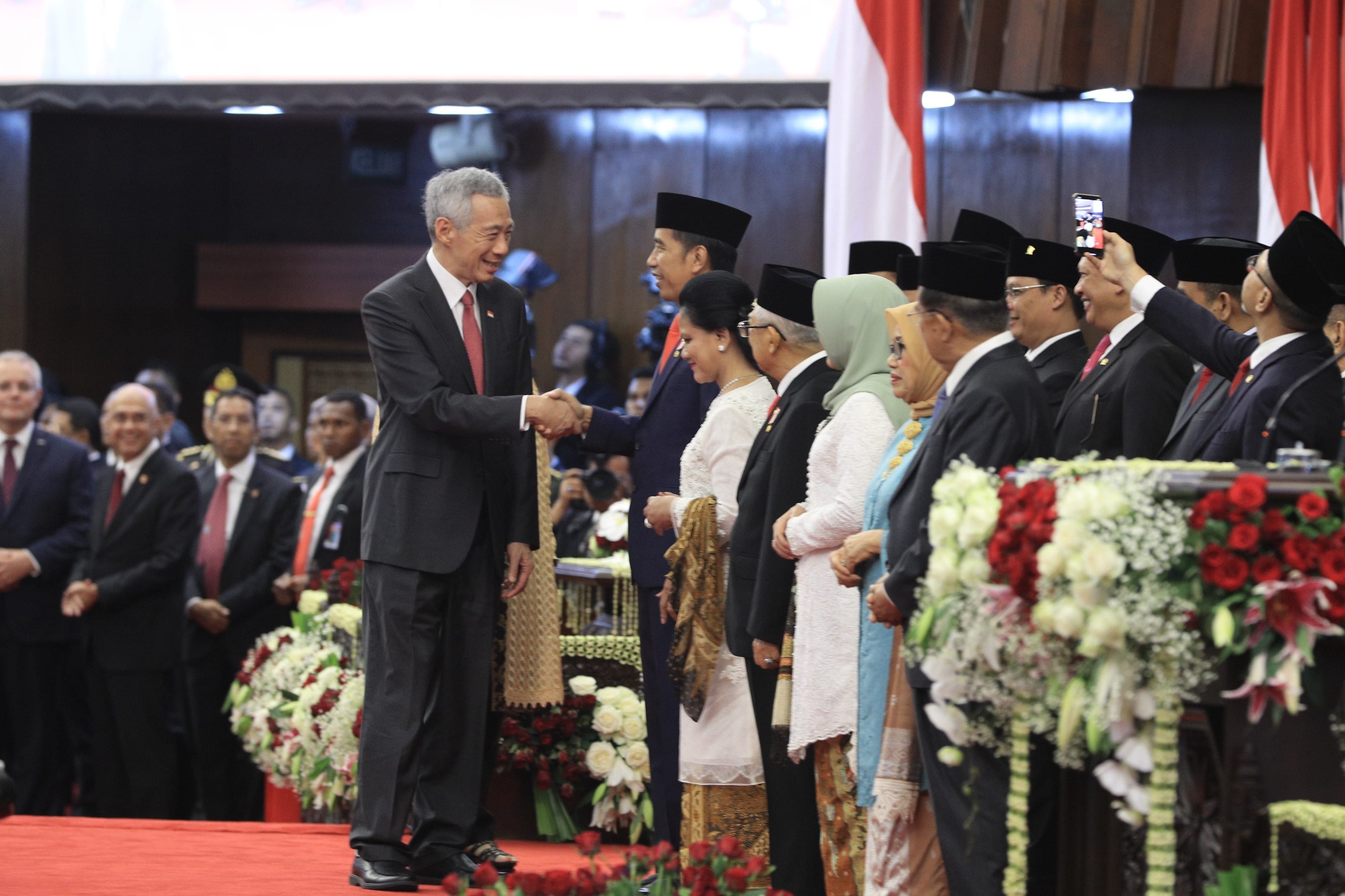 Lee Hsien Loong shakes hands with Jokowi amid a crowd at an official event.